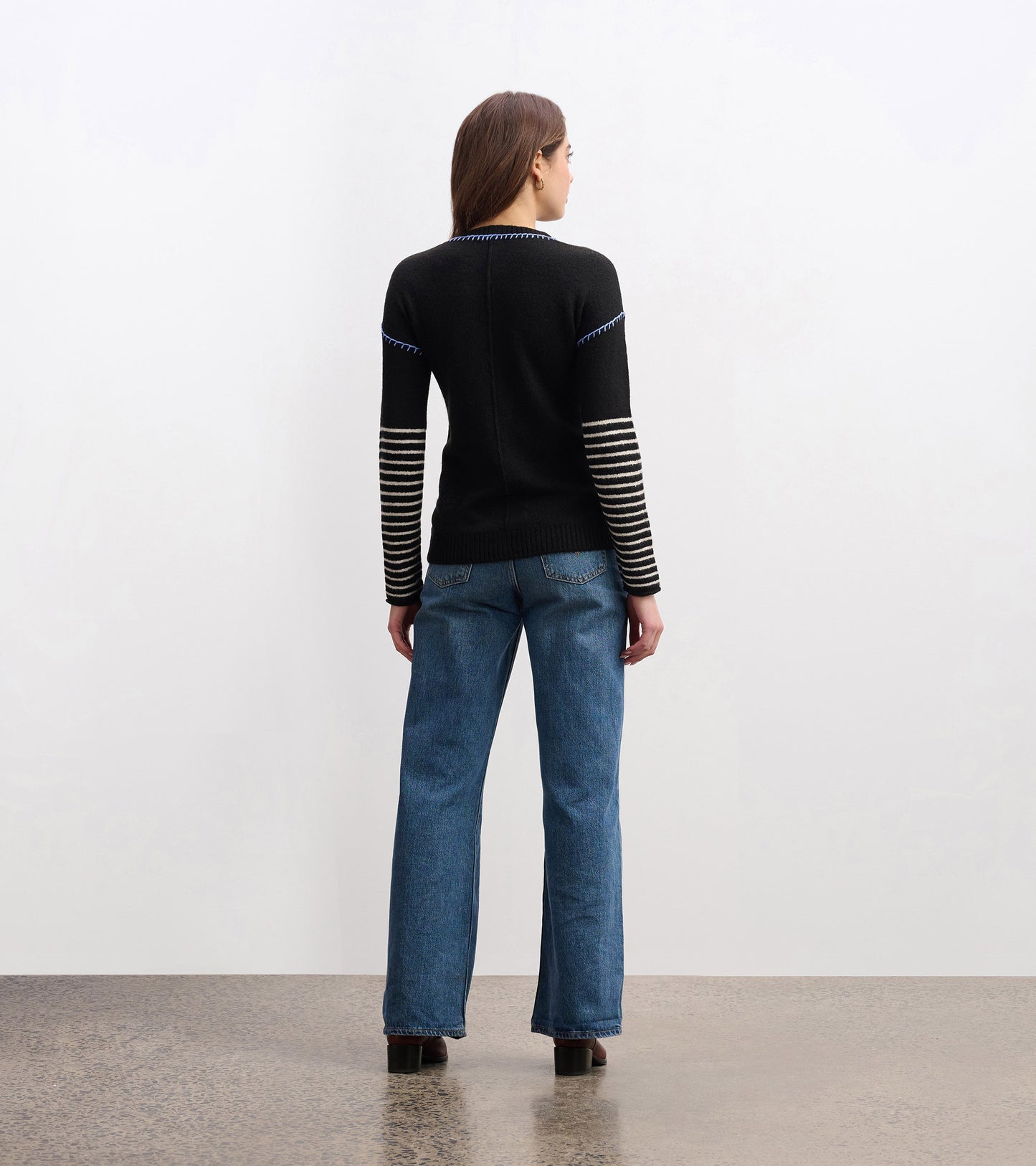 Black sweater with striped sleeves, fitted body, and a round neckline, worn with blue jeans, viewed from the back.