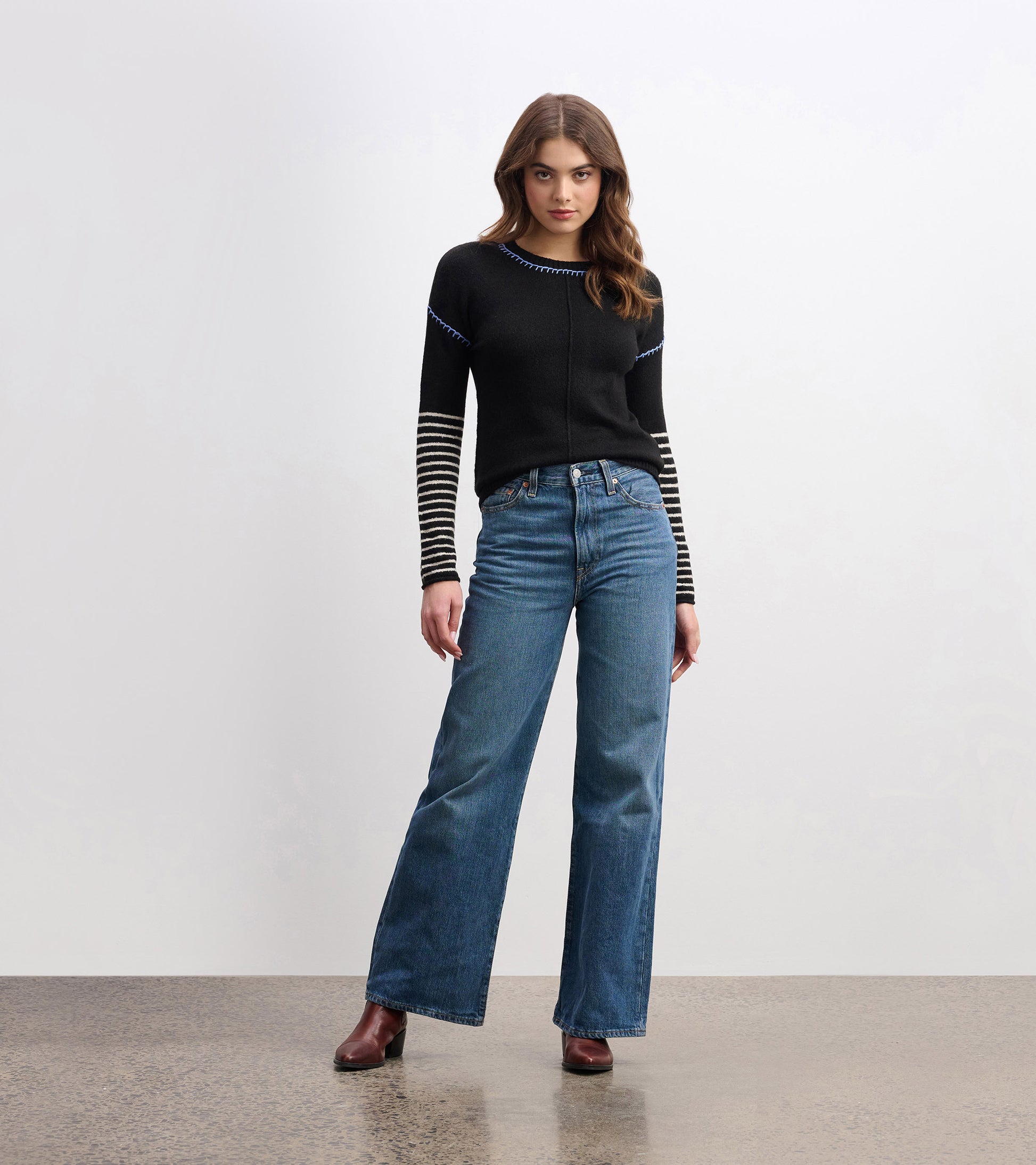 Black sweater with striped sleeves and blue detailing, paired with high-waisted jeans.