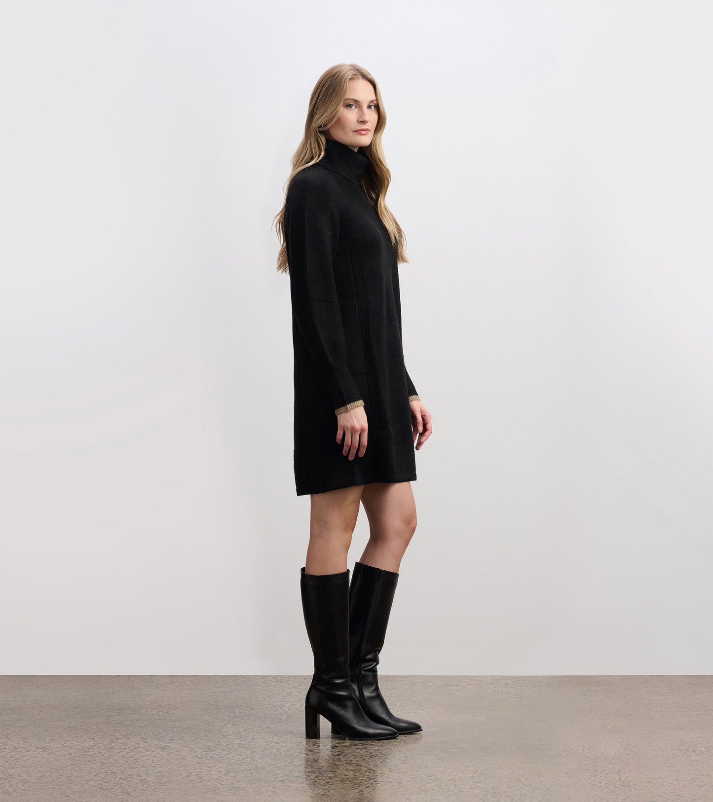 Black swing sweater dress with a high neckline and long sleeves, styled with knee-high black boots.