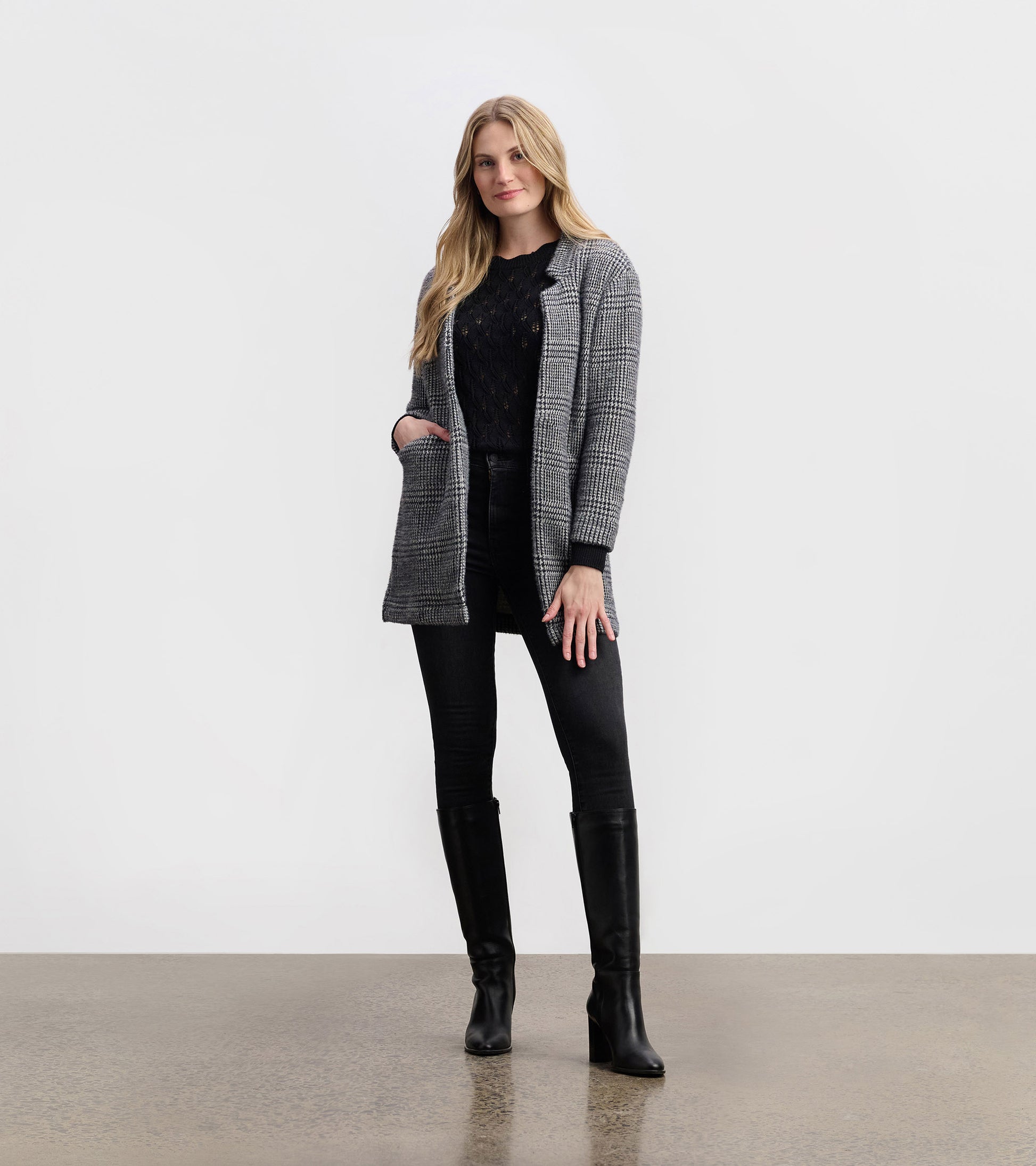 Cozy black check open blazer with pockets, styled over a black top and paired with black jeans and knee-high boots.
