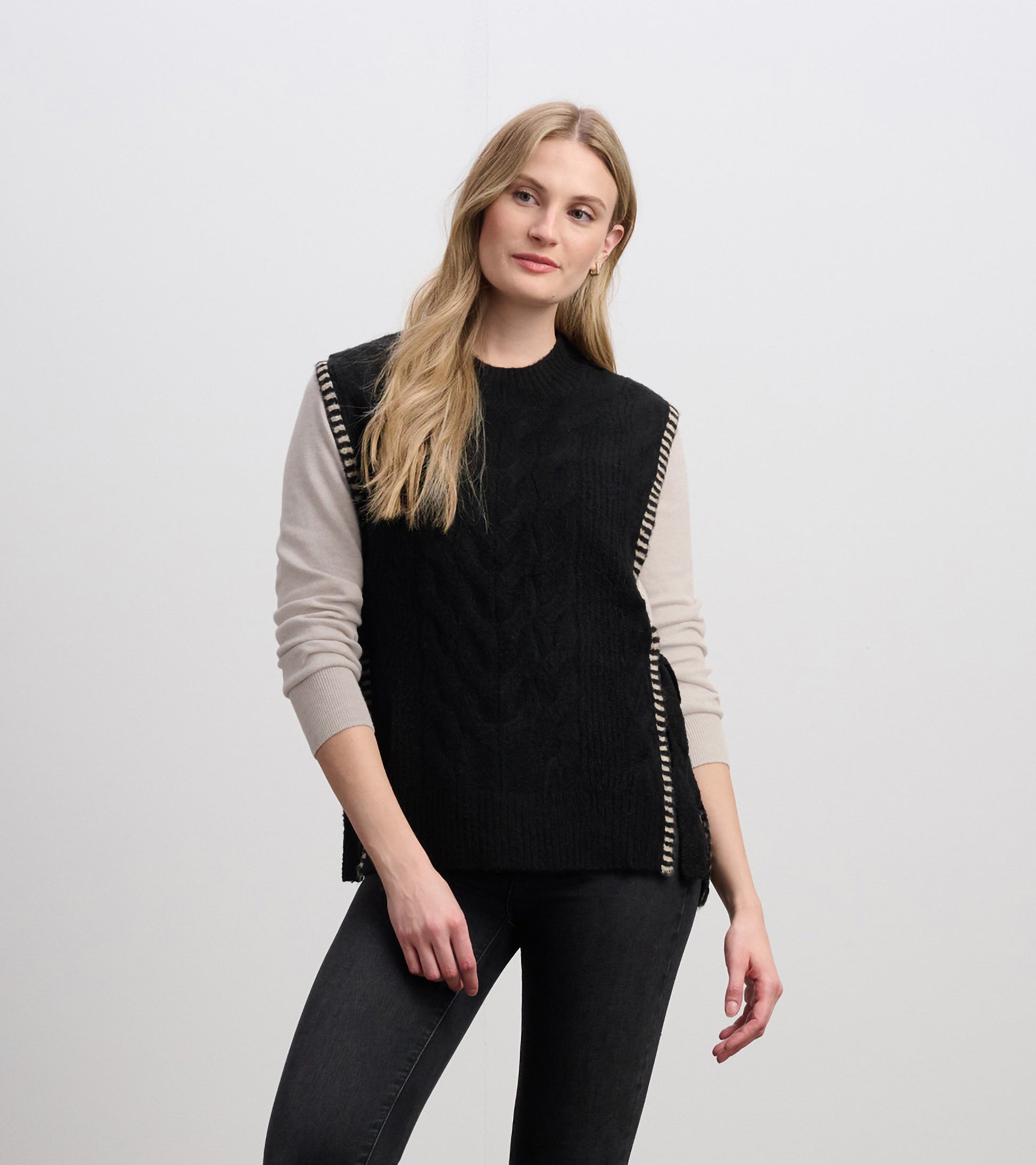 Black side-tie sweater vest with cable knit texture and striped detailing on the shoulders, styled over a light top.