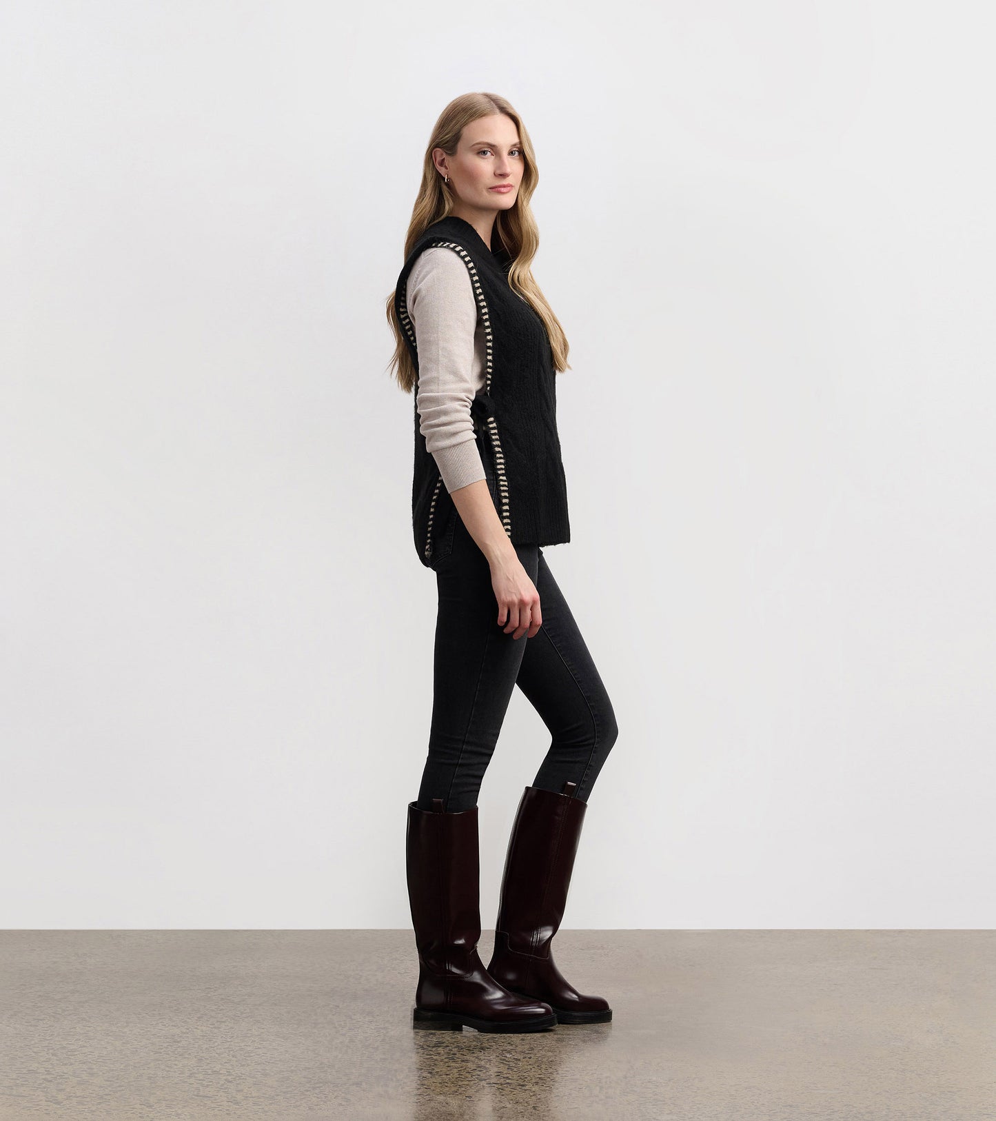 Black side-tie sweater vest with a textured pattern, styled over a light top and paired with dark jeans and tall boots.
