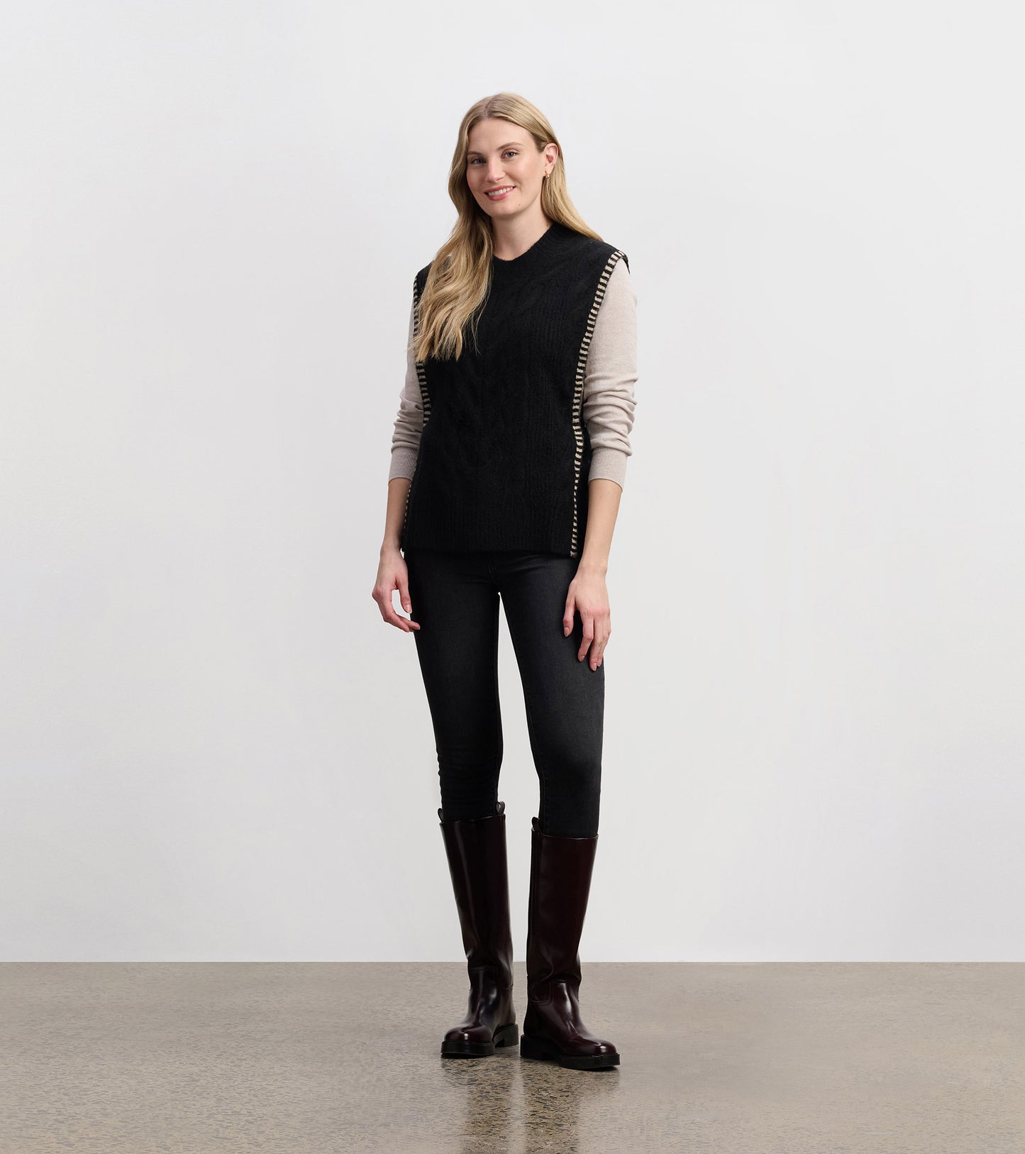 Black side-tie sweater vest with a textured pattern, styled over a light long-sleeve top and paired with dark jeans.