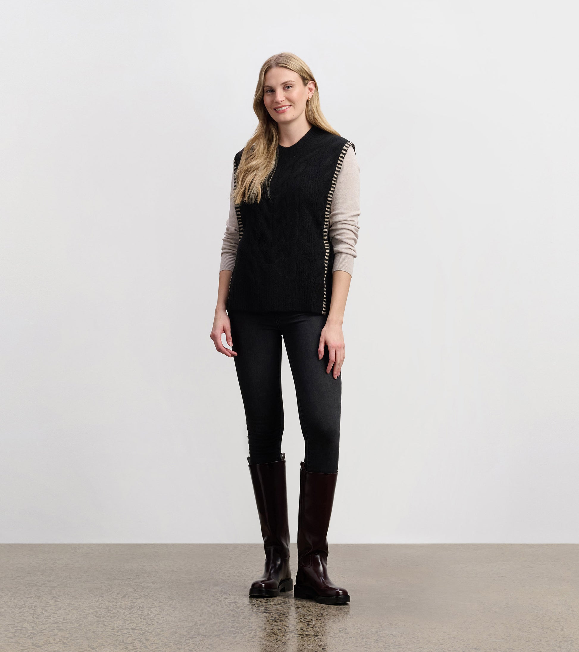Black side-tie sweater vest with a textured pattern, styled over a light long-sleeve top and paired with dark jeans.