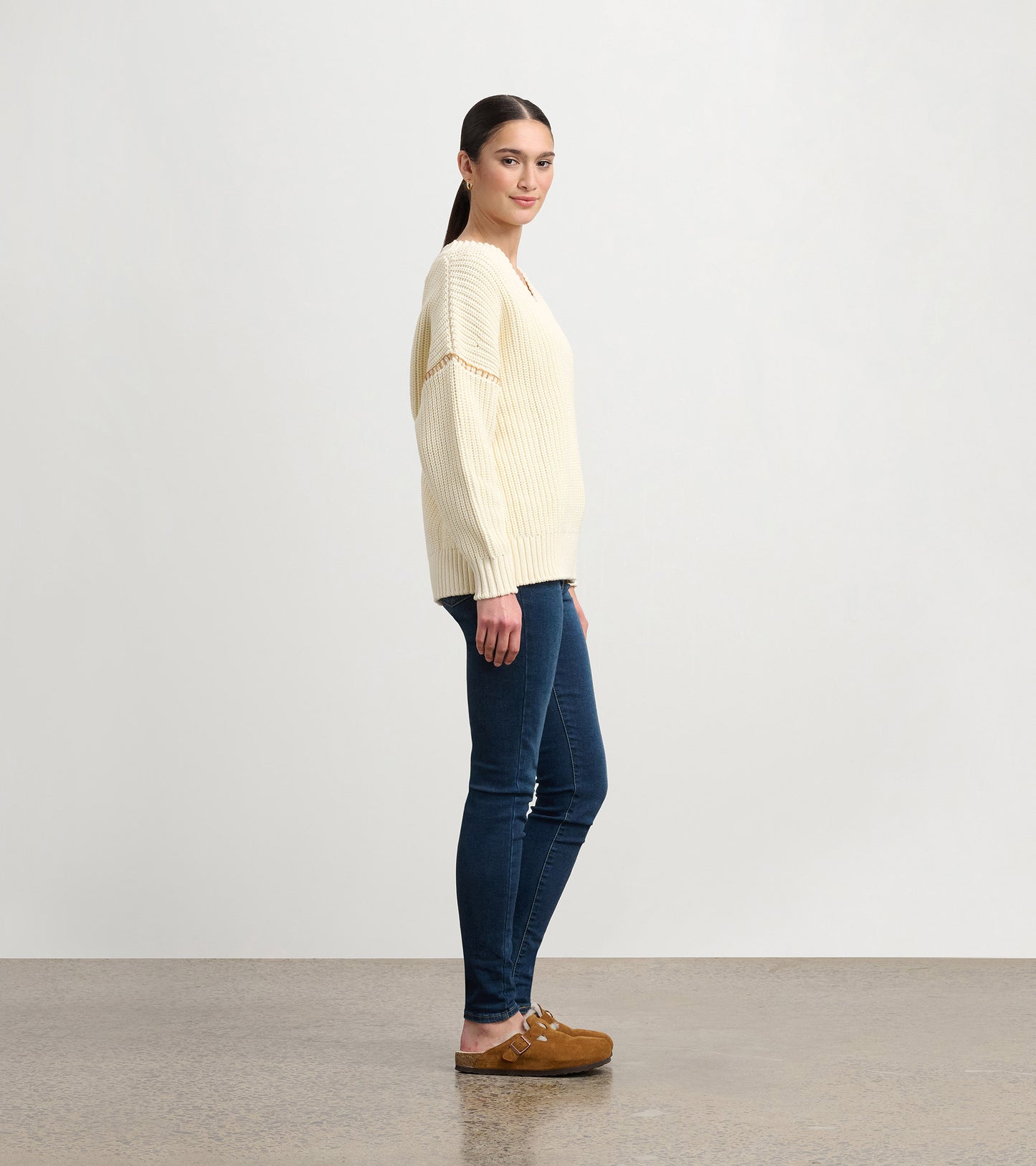 Cream V-neck slouchy sweater with ribbed texture, relaxed fit, and long sleeves, styled with dark jeans and clogs.