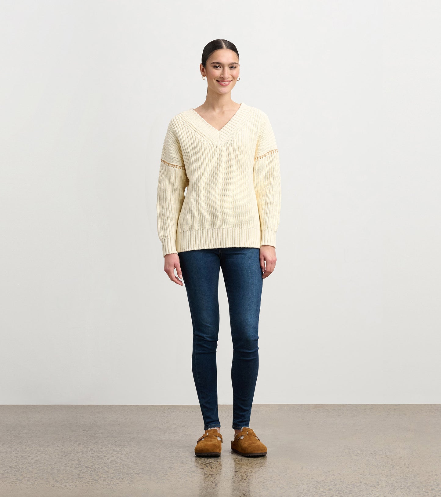 Cream V-neck slouchy sweater with ribbed texture and long sleeves, styled with dark jeans and brown footwear.