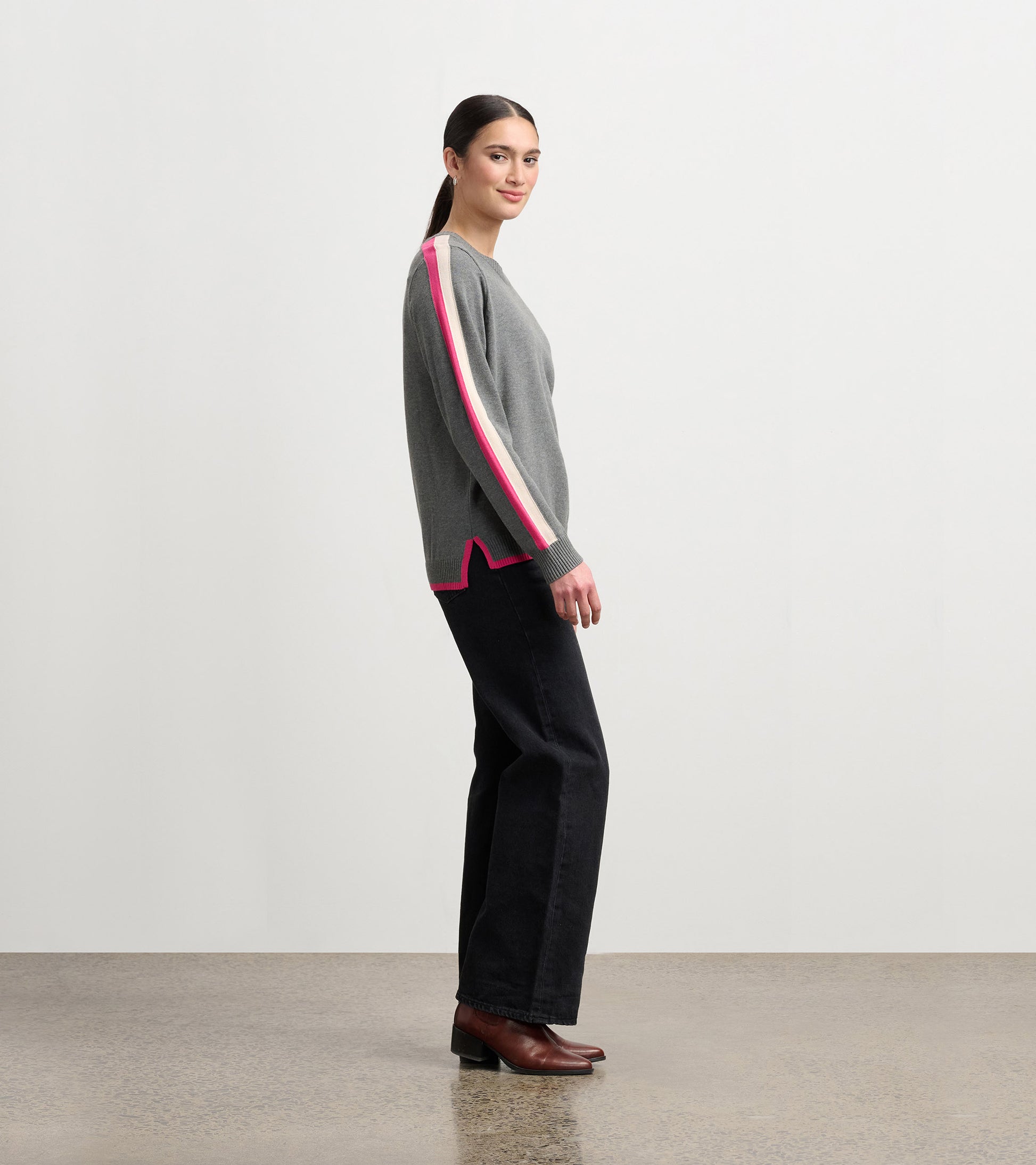 Charcoal sweater with pink and white contrast trim, featuring a relaxed fit and side slits, worn with black pants.