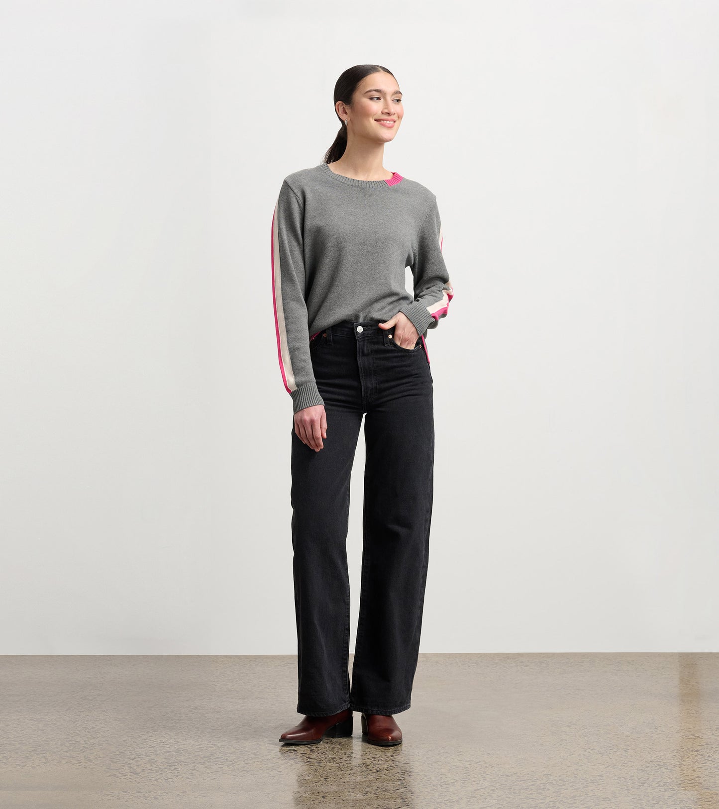 Charcoal sweater with contrasting pink trim, crew neck, and relaxed fit, paired with high-waisted black jeans.