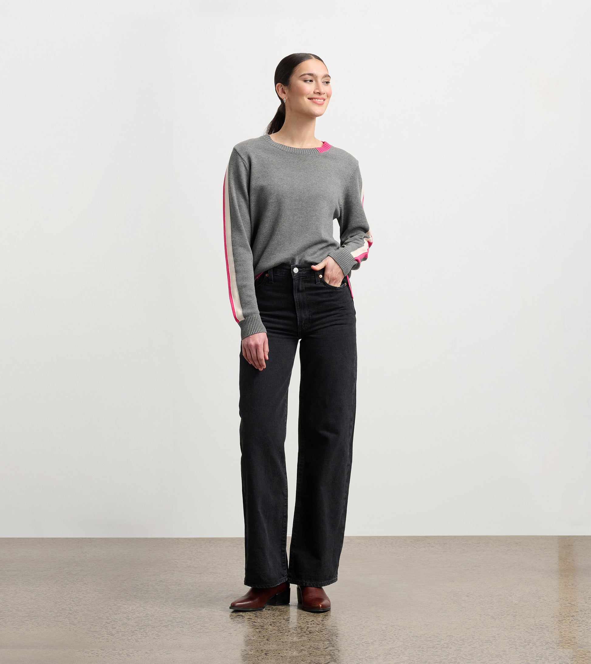 Charcoal sweater with contrasting pink trim, crew neck, and relaxed fit, paired with high-waisted black jeans.