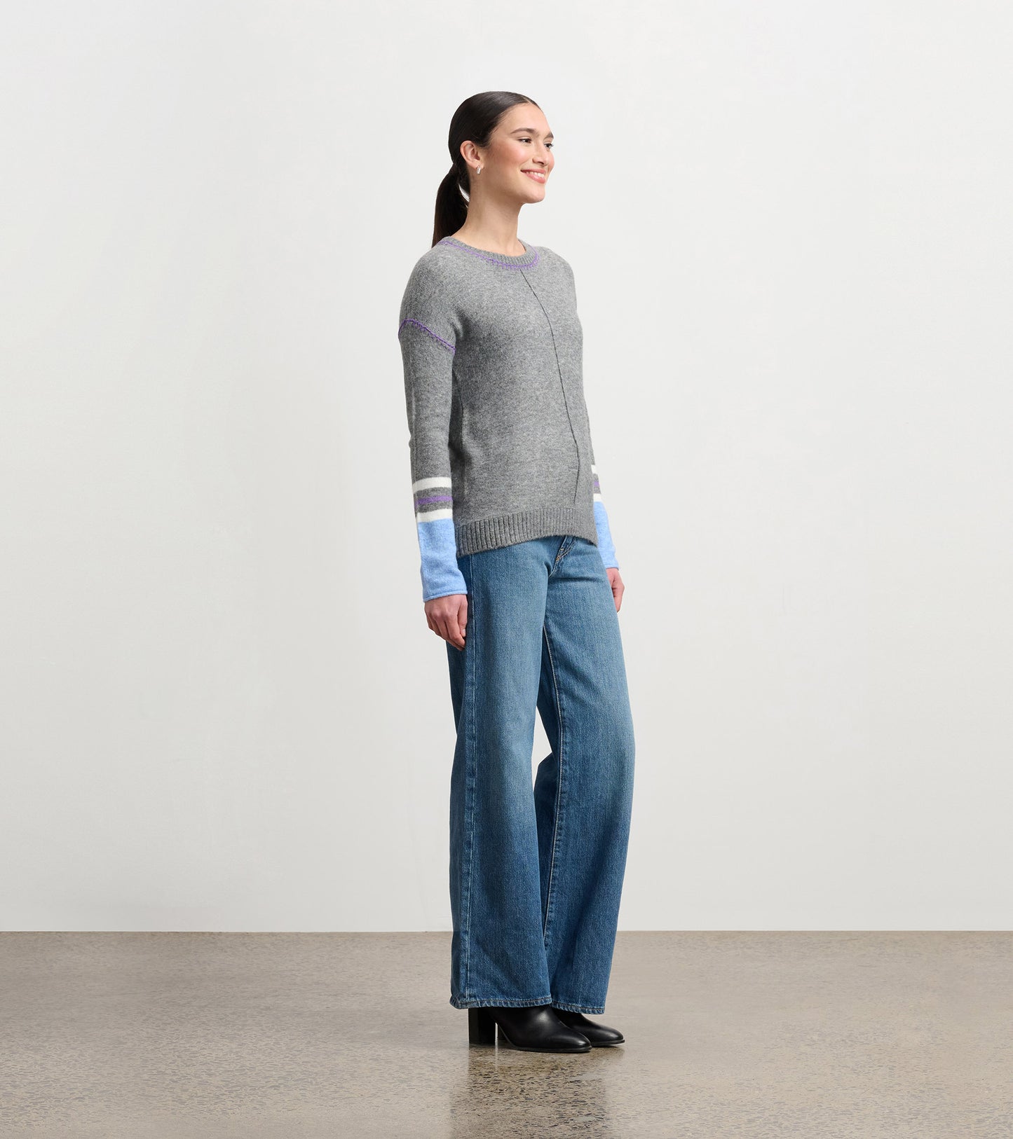 Charcoal melange sweater with colorful striped sleeves, paired with wide-leg jeans, shown from the side.