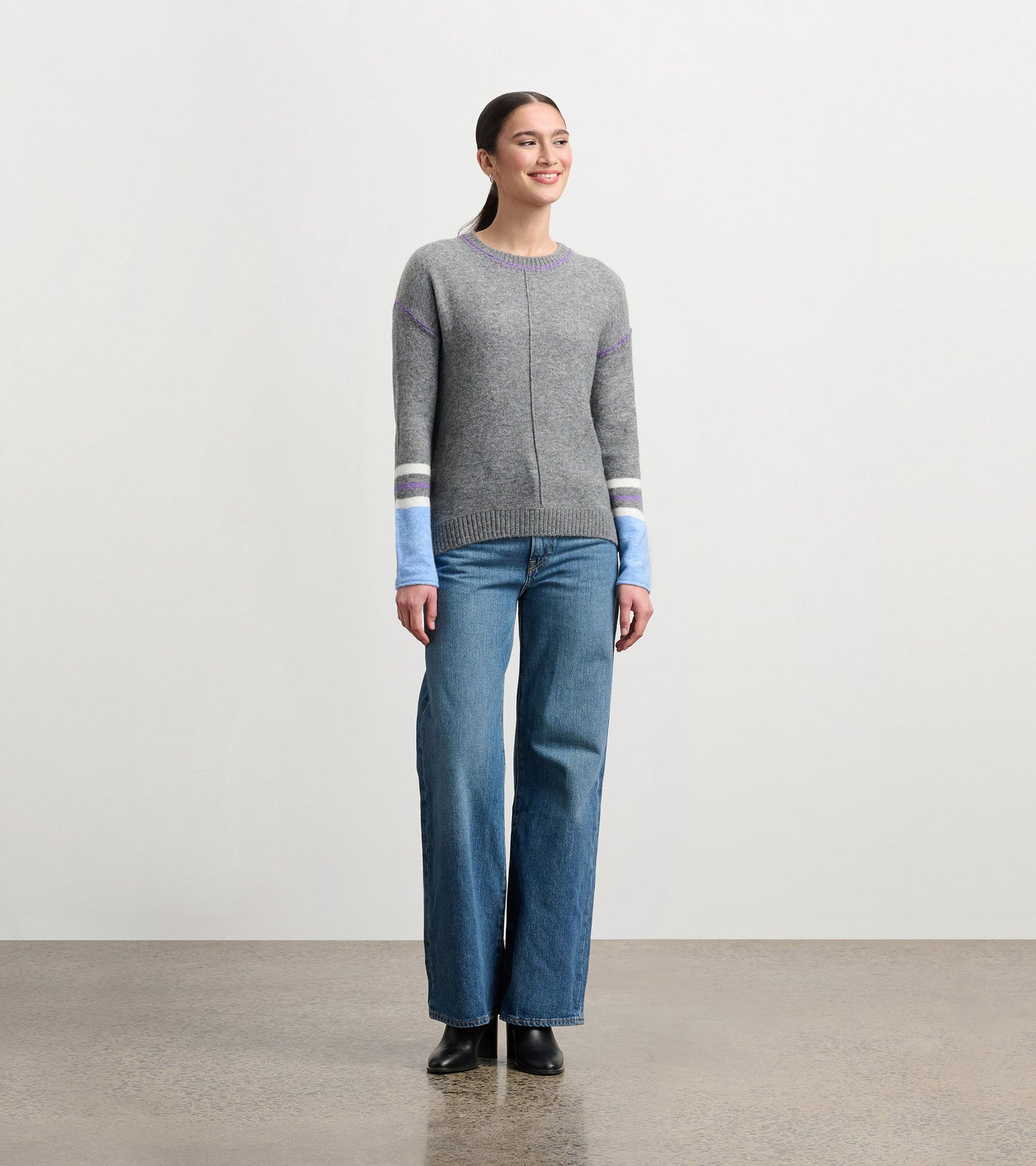 Charcoal melange sweater with purple and blue striped sleeves, round neckline, and relaxed fit, worn with wide-leg jeans.
