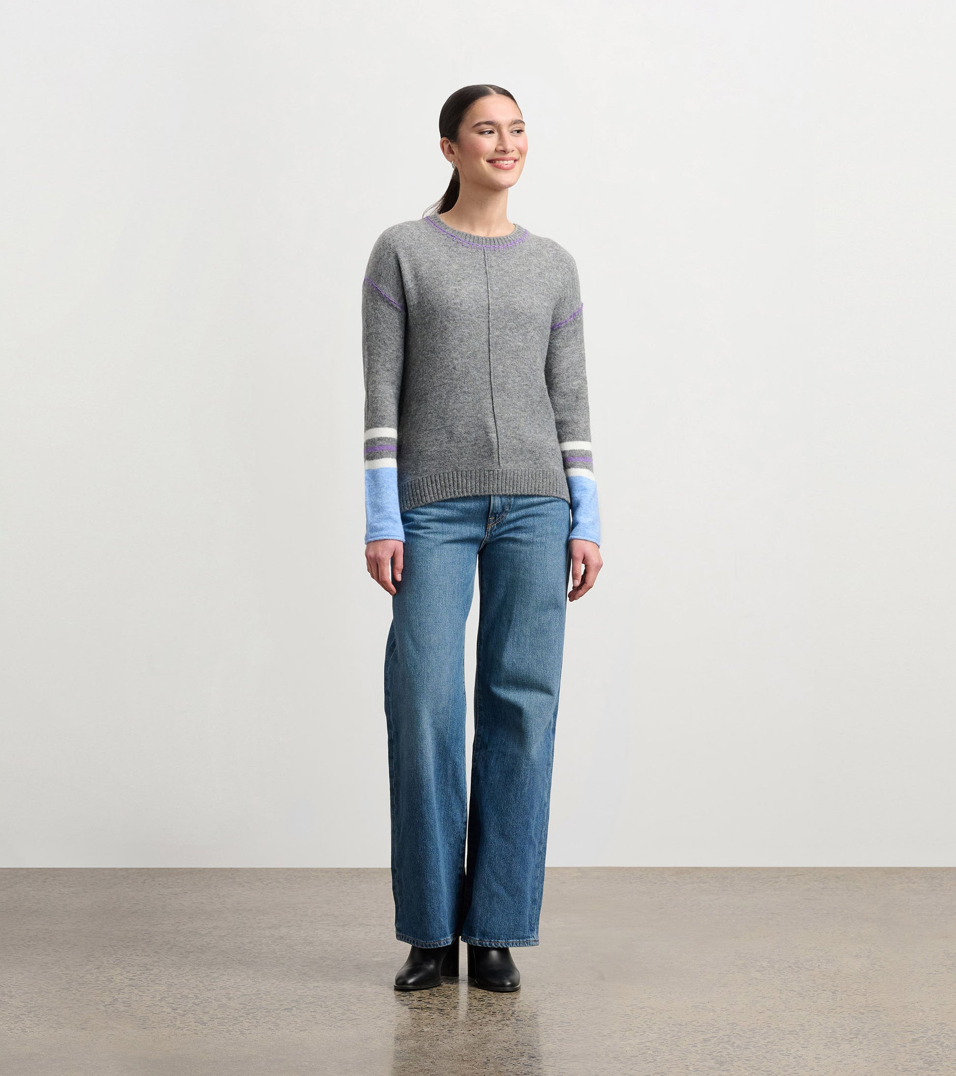 Charcoal melange sweater with purple and blue striped sleeves, round neckline, and relaxed fit, worn with wide-leg jeans.