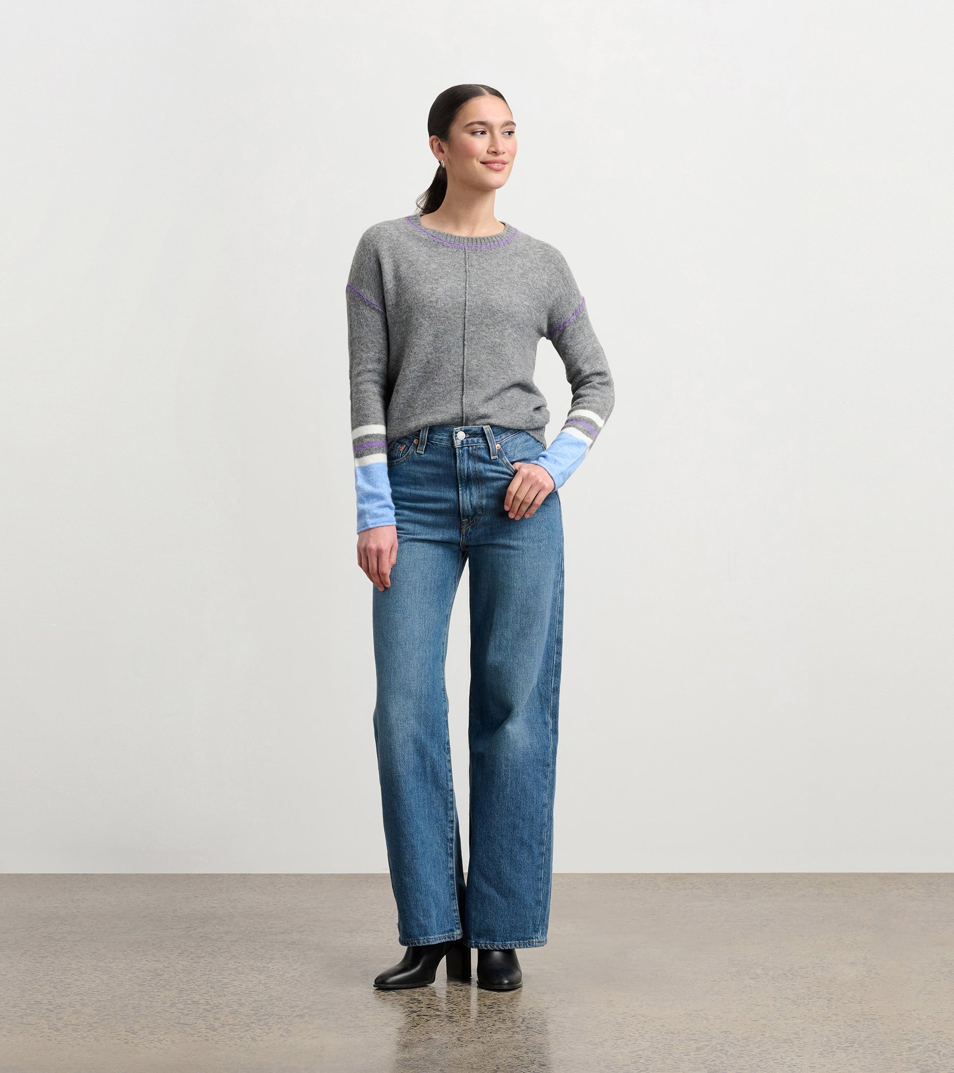 Charcoal melange sweater with colorful striped sleeves, worn with high-waisted jeans and heeled boots.