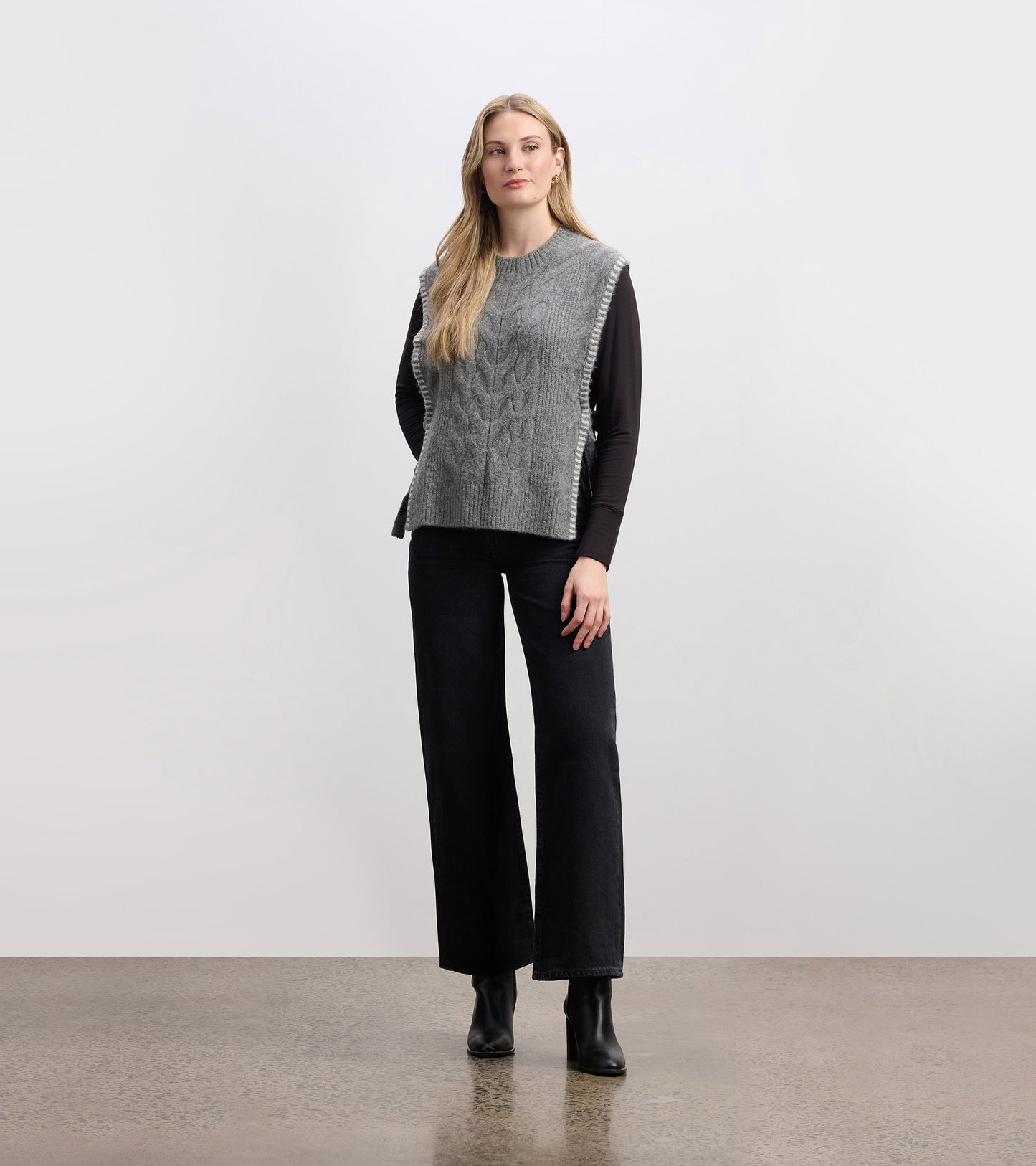 Charcoal melange side-tie sweater vest with a textured knit pattern, styled over a long-sleeve top and paired with wide-leg…