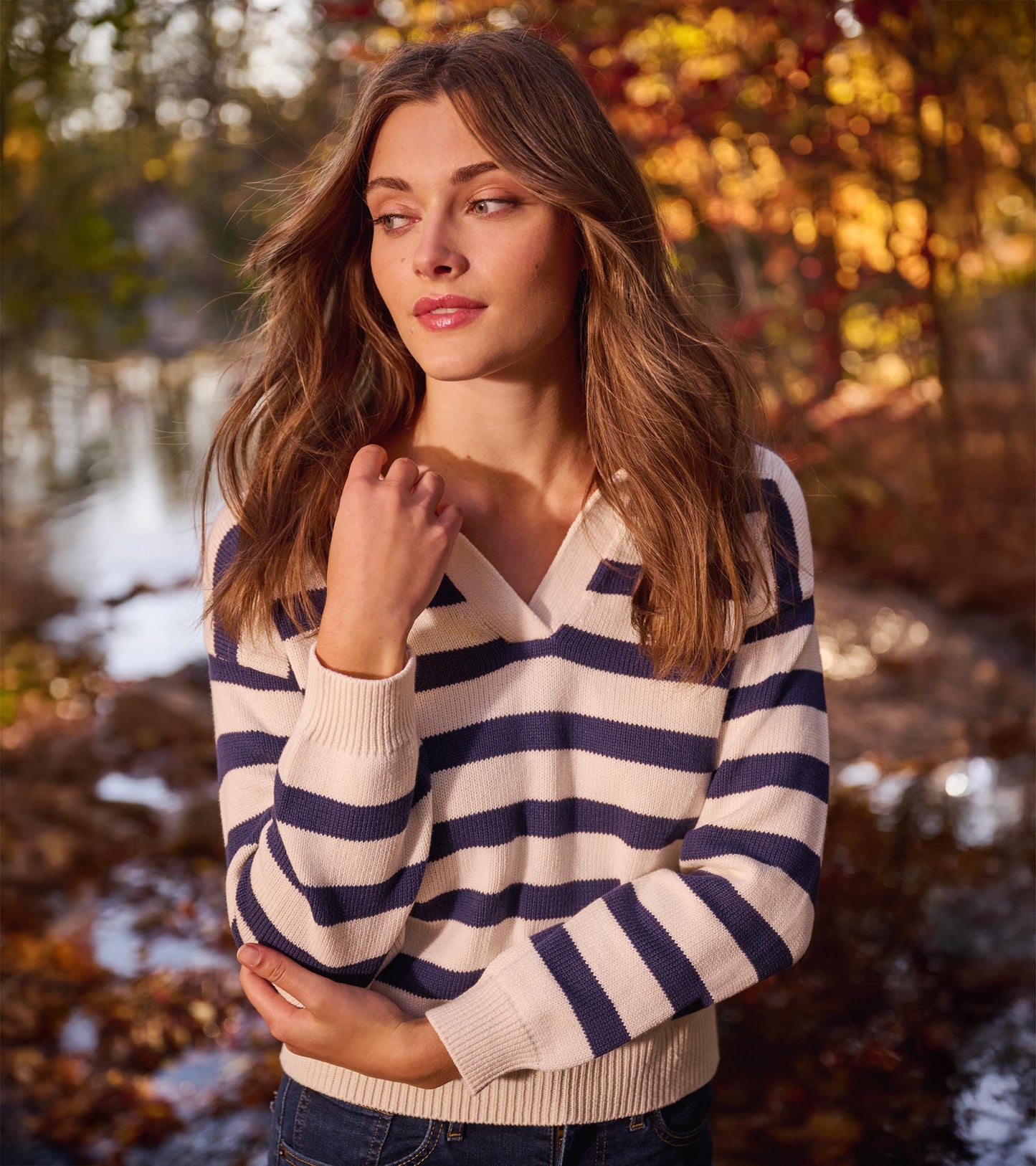 Cream and navy striped V-neck sweater with ribbed cuffs and hem, worn by a woman outdoors.