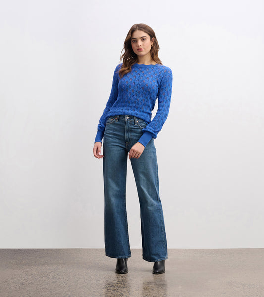 Denim blue knitted sweater with a textured pattern, featuring long sleeves and a round neckline, paired with wide-leg jeans.
