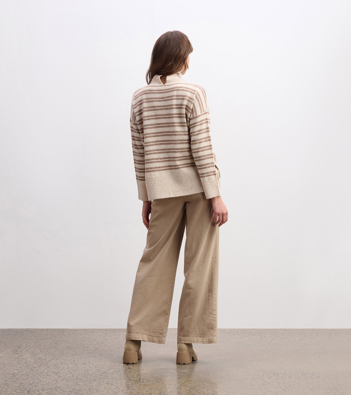 Mock neck sweater in camel with double stripes, featuring a relaxed fit and ribbed hem, styled with wide-leg pants.