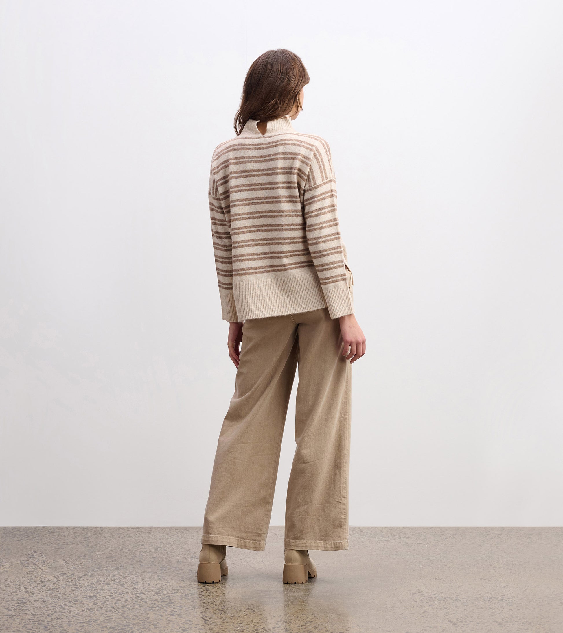 Mock neck sweater in camel with double stripes, featuring a relaxed fit and ribbed hem, styled with wide-leg pants.