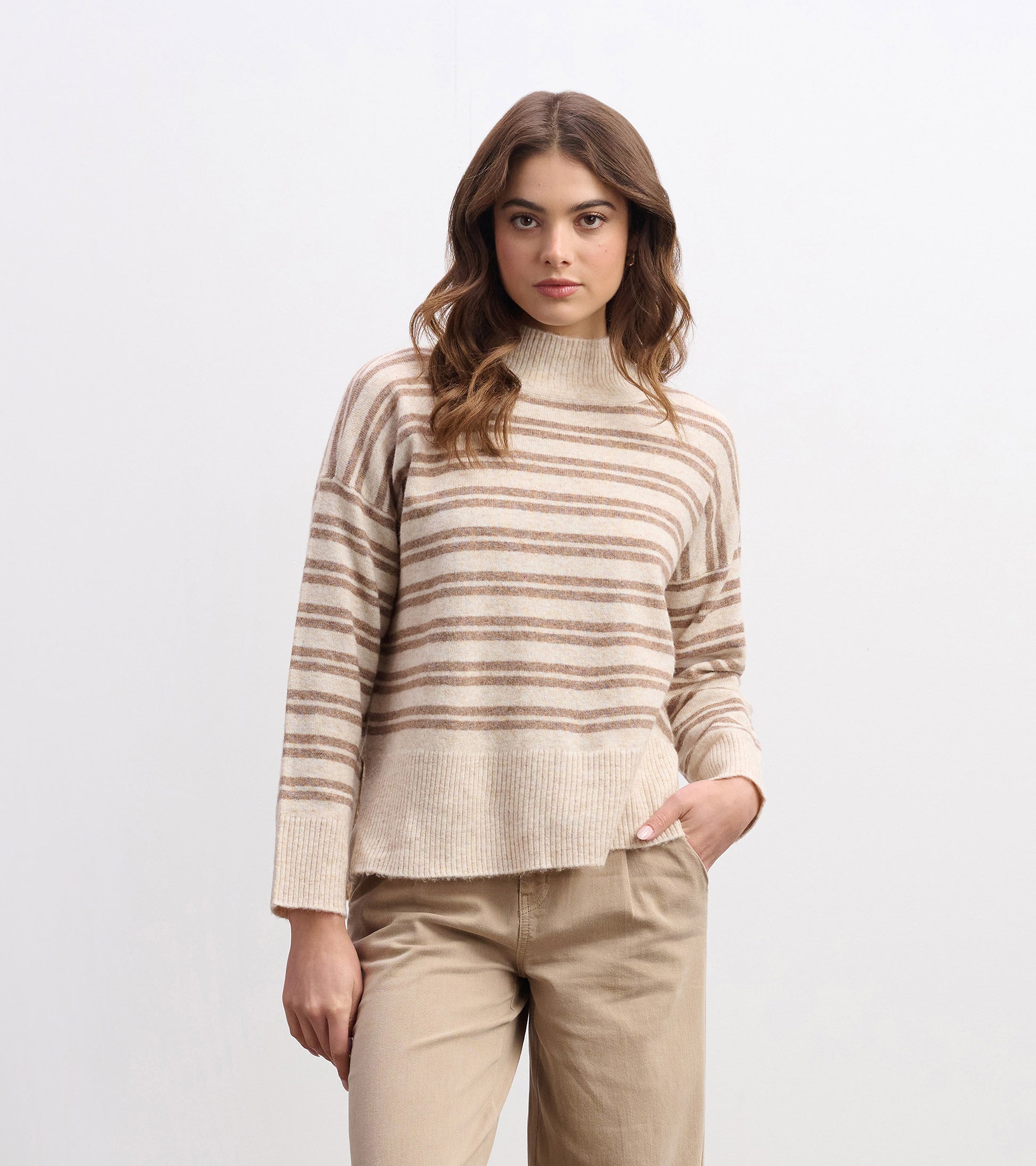 Mock neck sweater in camel with double stripes, featuring a relaxed fit and ribbed hem, styled with beige pants.