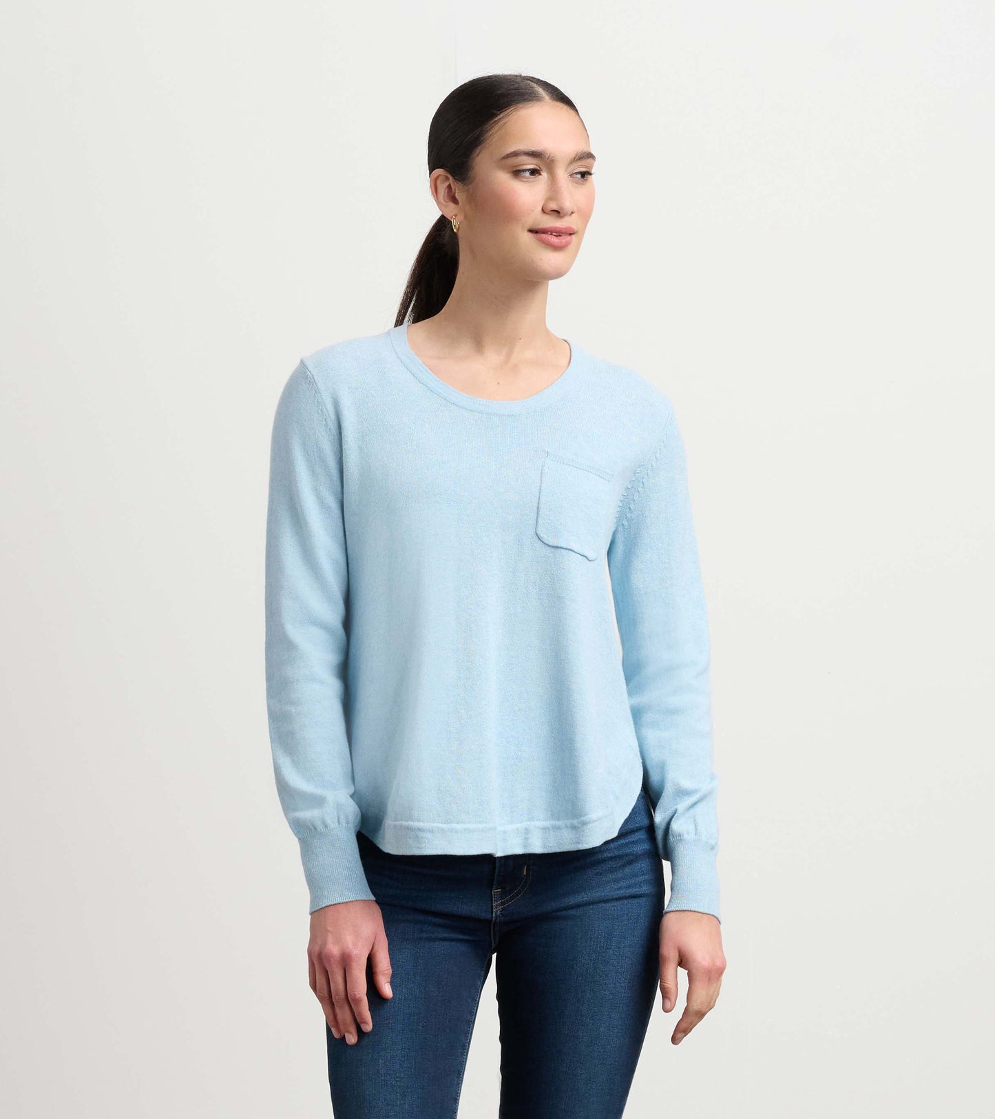 Light blue sweater with long sleeves and a front pocket, styled with fitted jeans.