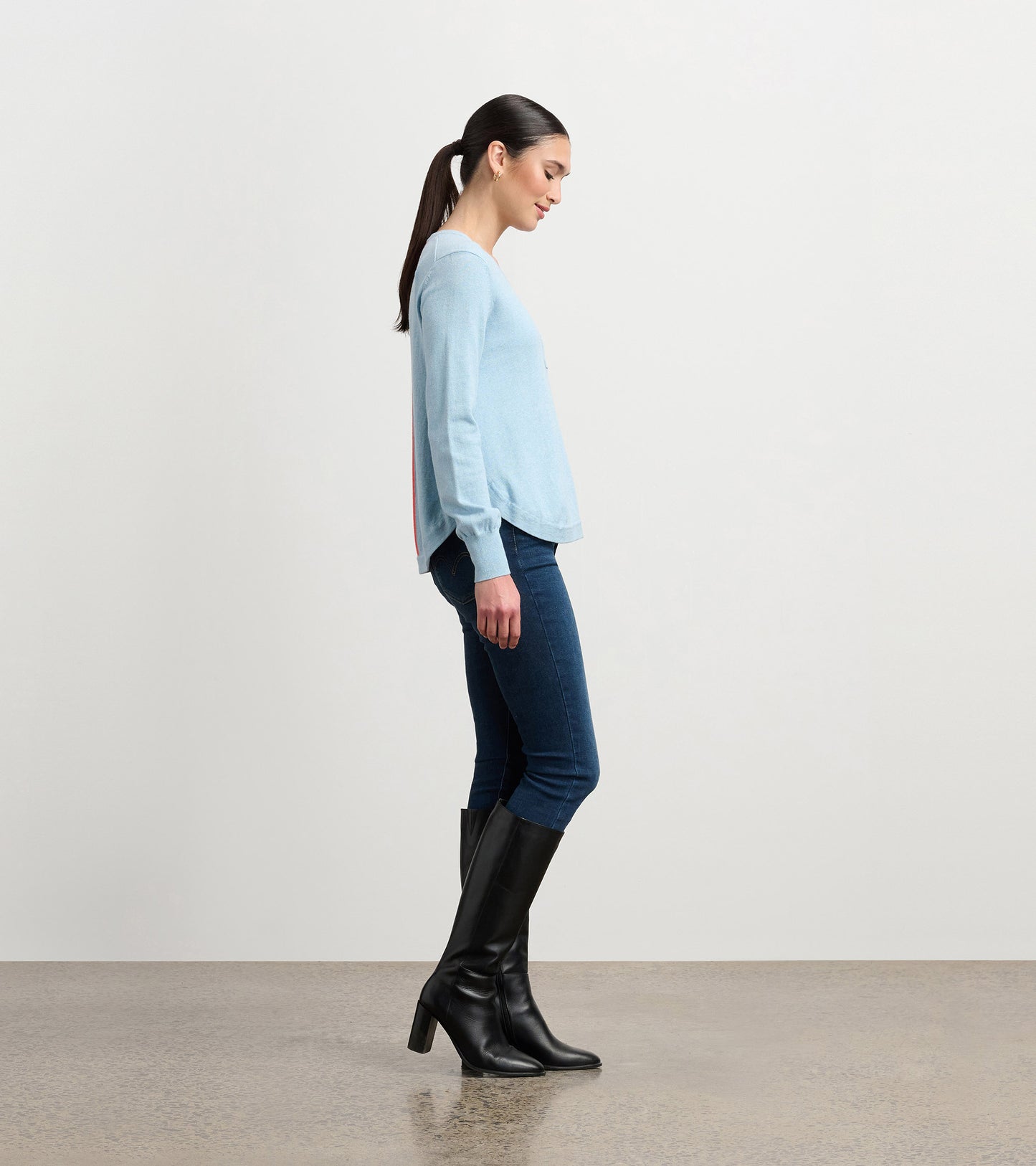 Light blue sweater with long sleeves, side slit detail, paired with dark jeans and knee-high black boots. Side view.