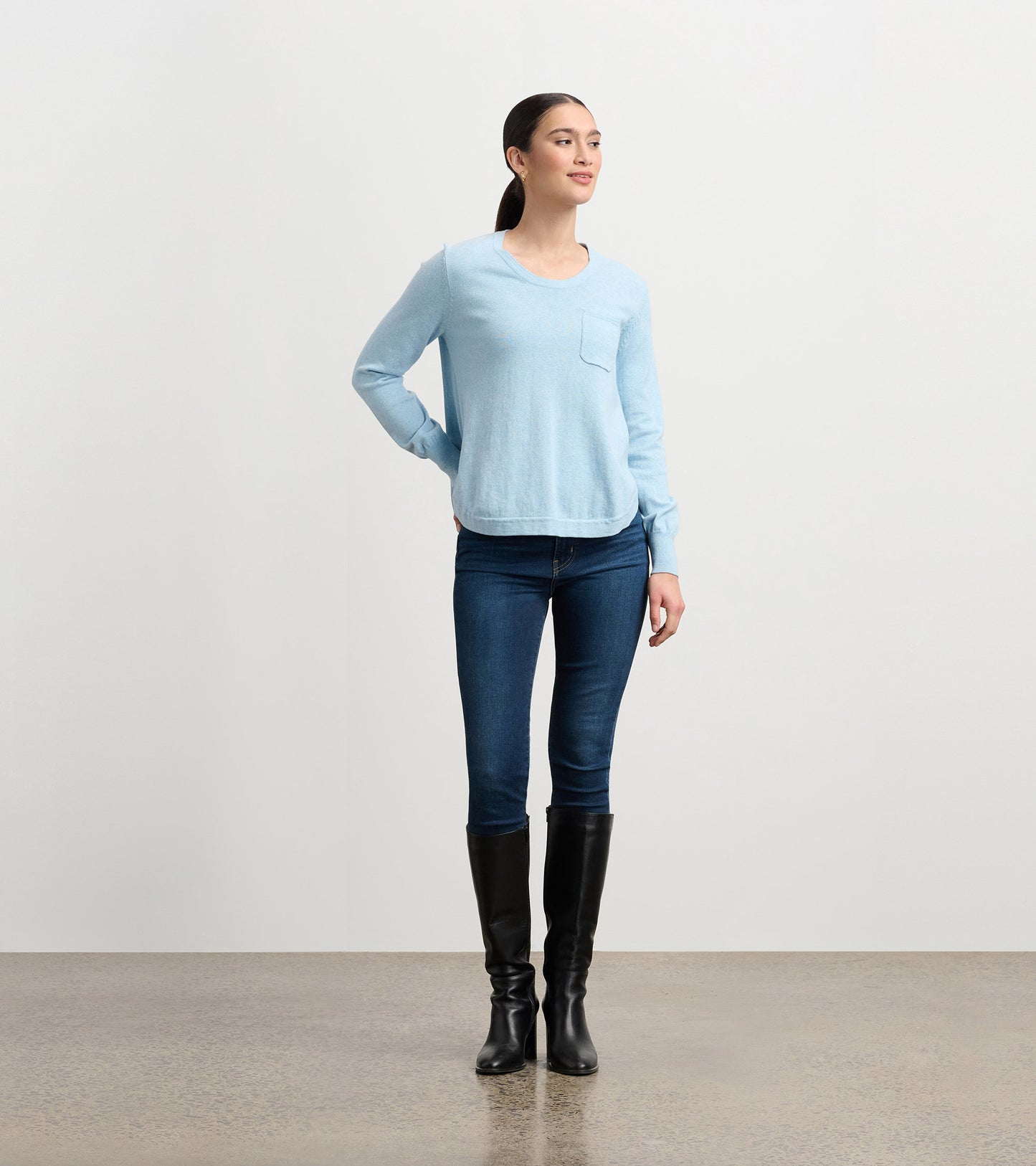 Light blue long-sleeve sweater with a front pocket, paired with dark jeans and knee-high black boots.