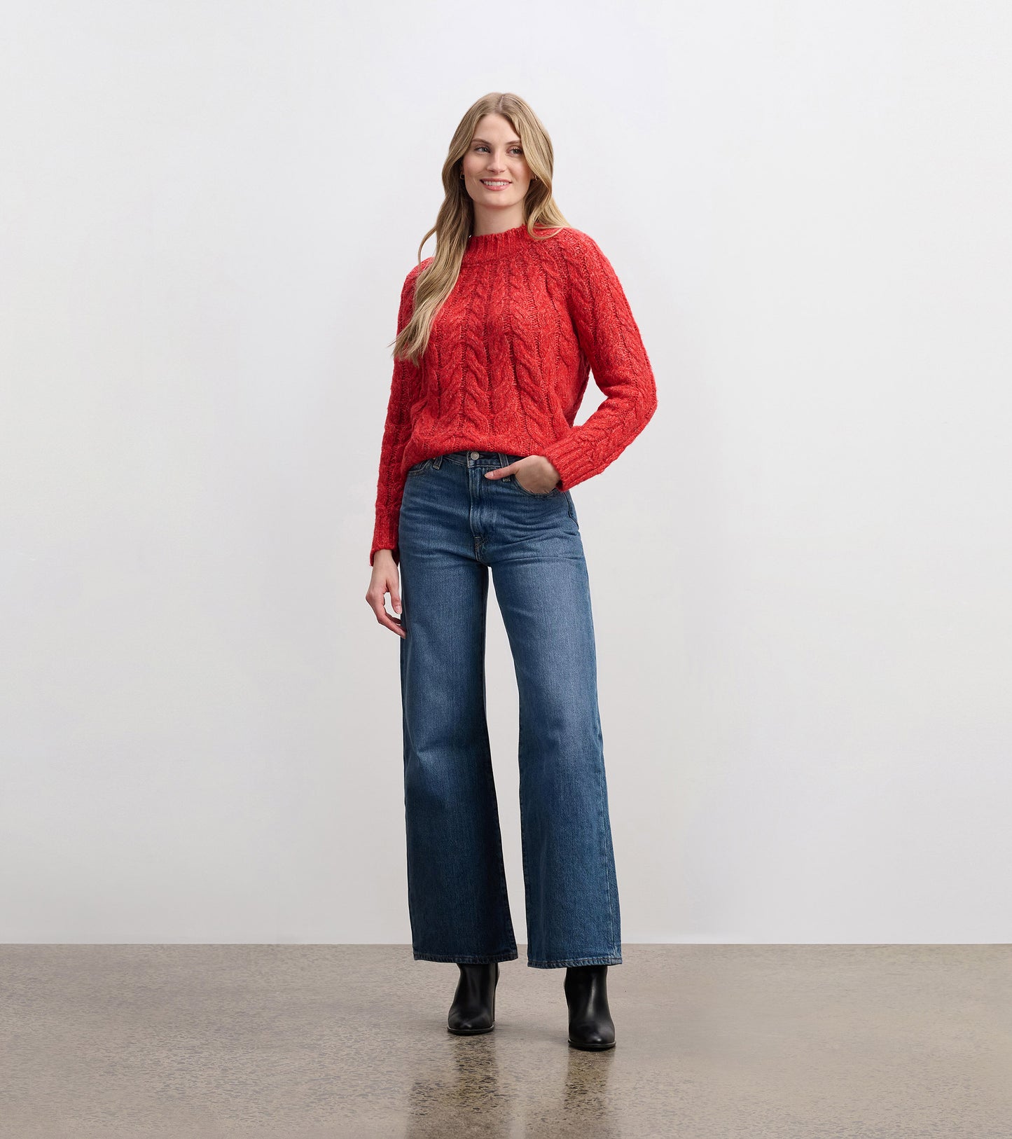 Red cable knit sweater with a round neckline, worn with high-waisted wide-leg jeans and ankle boots.