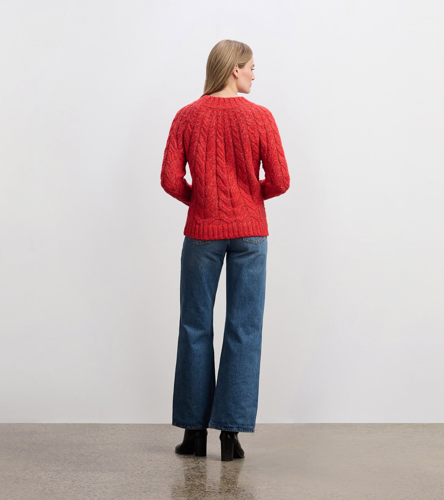 Red cable knit sweater with a relaxed fit, featuring a round neckline and long sleeves, styled with wide-leg jeans.