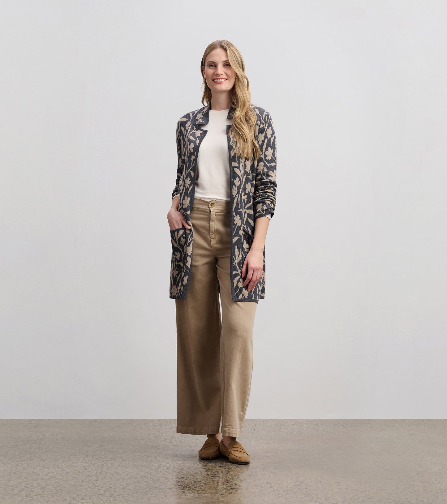 Floral vine patterned sweater blazer in navy and cream, featuring an open front and side pockets, styled with beige pants.