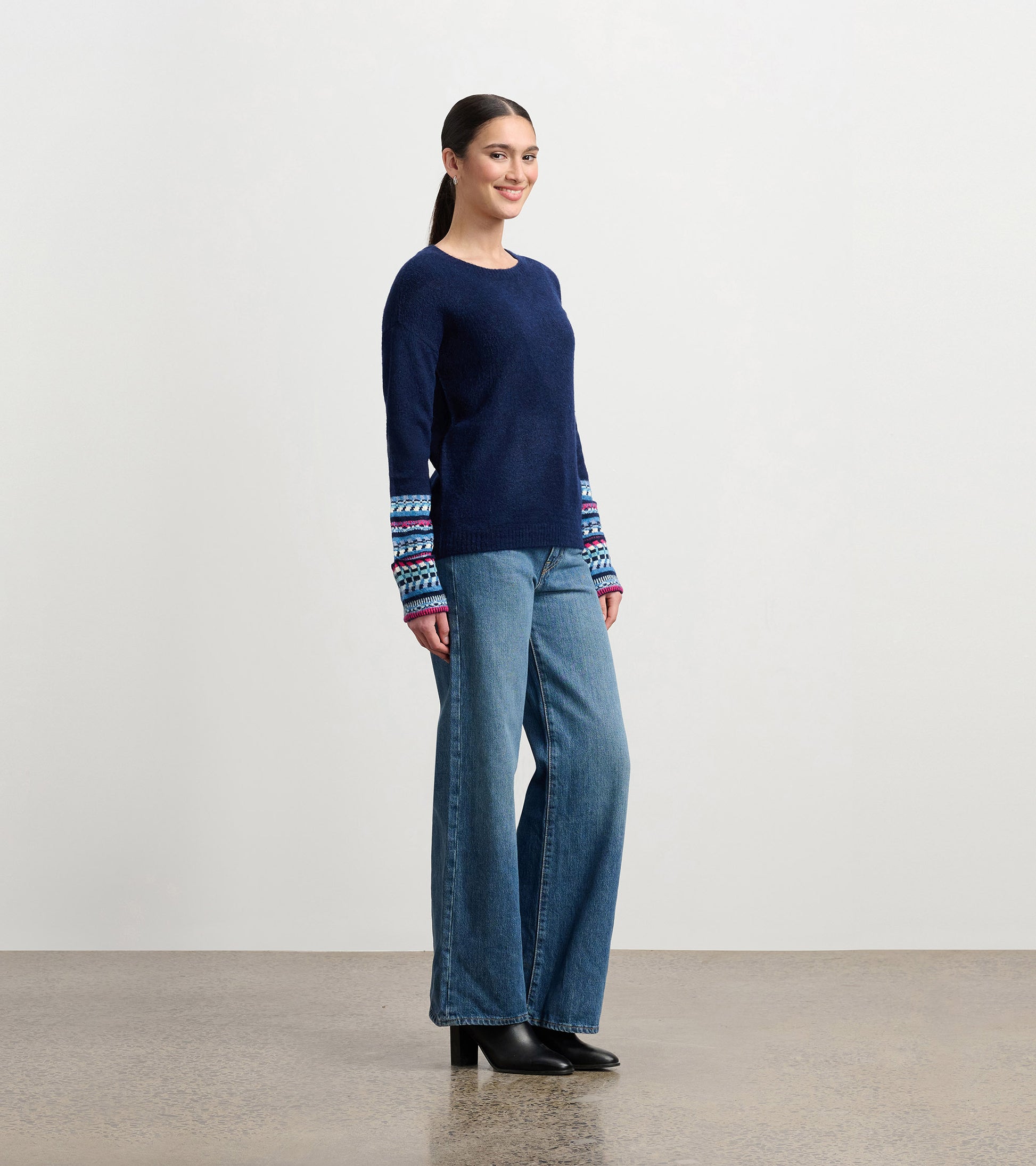 Navy sweater with colorful jacquard cuffs, paired with wide-leg jeans, shown from the side.