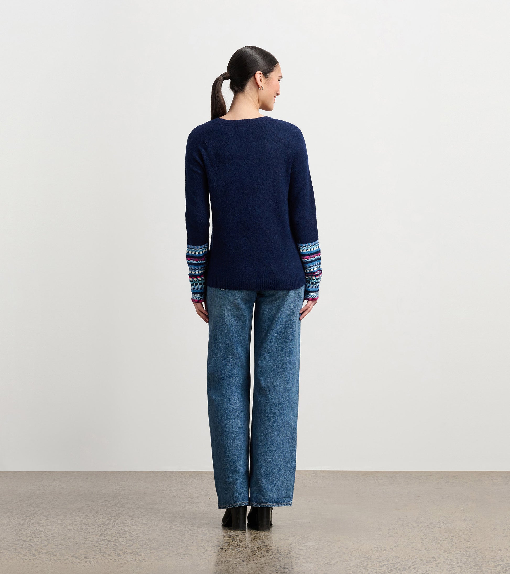 Navy sweater with colorful jacquard cuffs, featuring a relaxed fit and long sleeves, worn with wide-leg jeans.