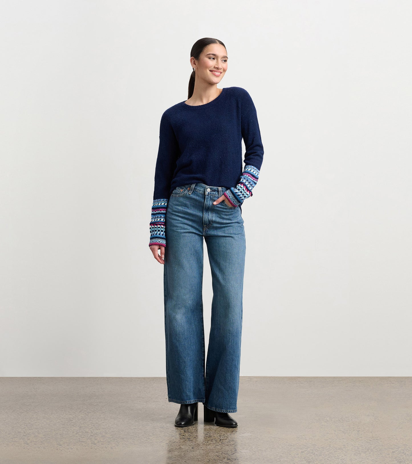 Navy sweater with colorful jacquard cuffs, paired with high-waisted jeans, worn by a model standing and smiling.