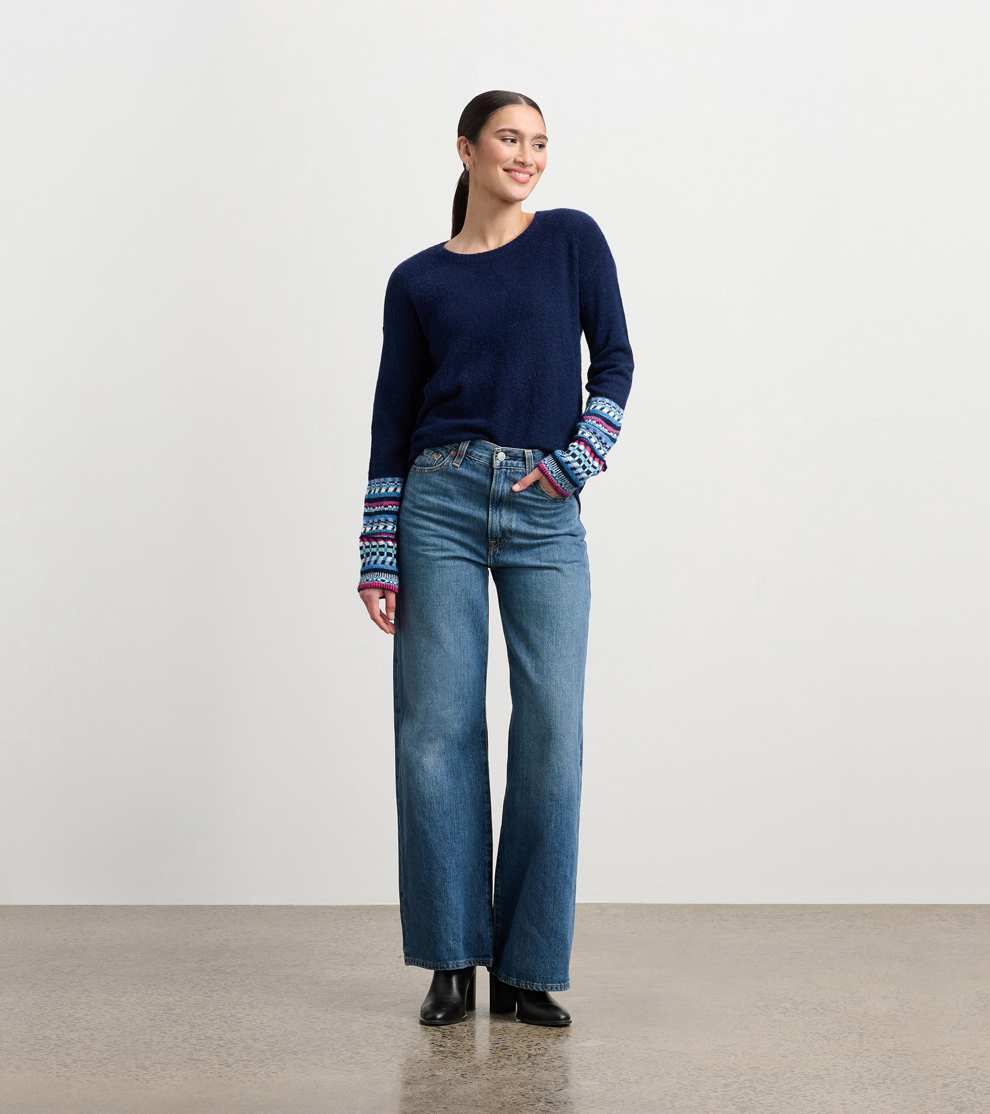 Navy sweater with colorful jacquard cuffs, paired with high-waisted jeans, worn by a model standing and smiling.