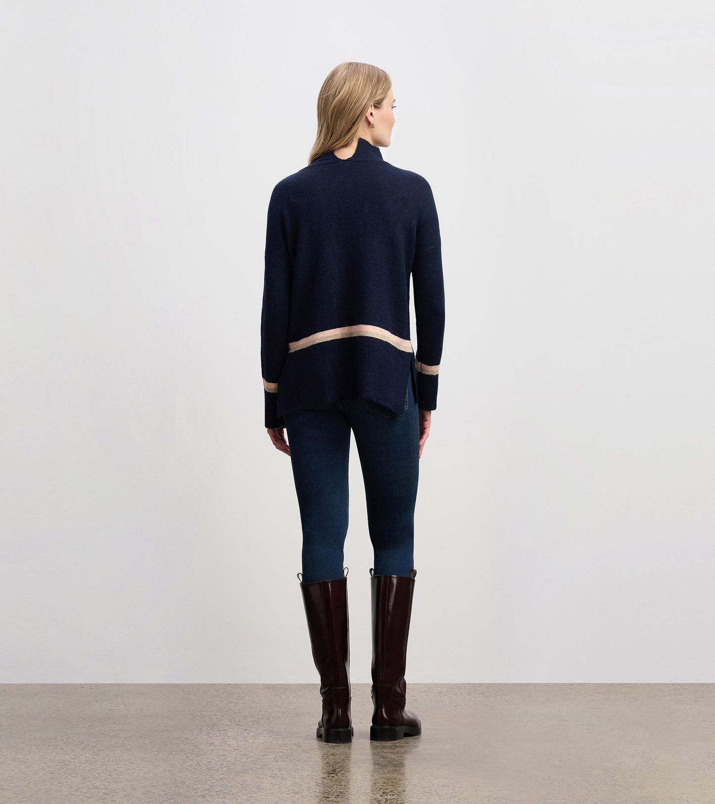 Navy mock neck sweater with a striped hem, featuring a relaxed fit and side slits, worn with dark jeans and tall boots.