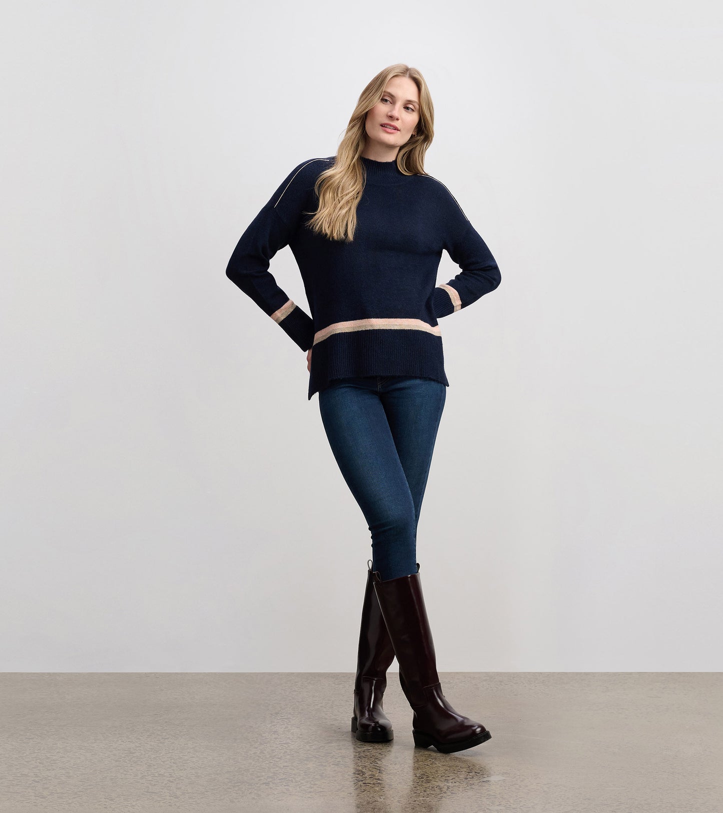 Navy mock neck sweater with cream stripes, featuring a relaxed fit and ribbed hem, styled with jeans and knee-high boots.