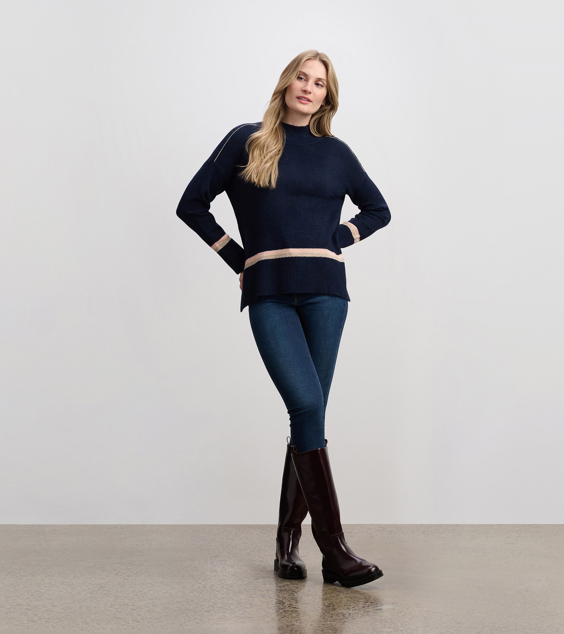 Navy mock neck sweater with cream stripes, featuring a relaxed fit and ribbed hem, styled with jeans and knee-high boots.
