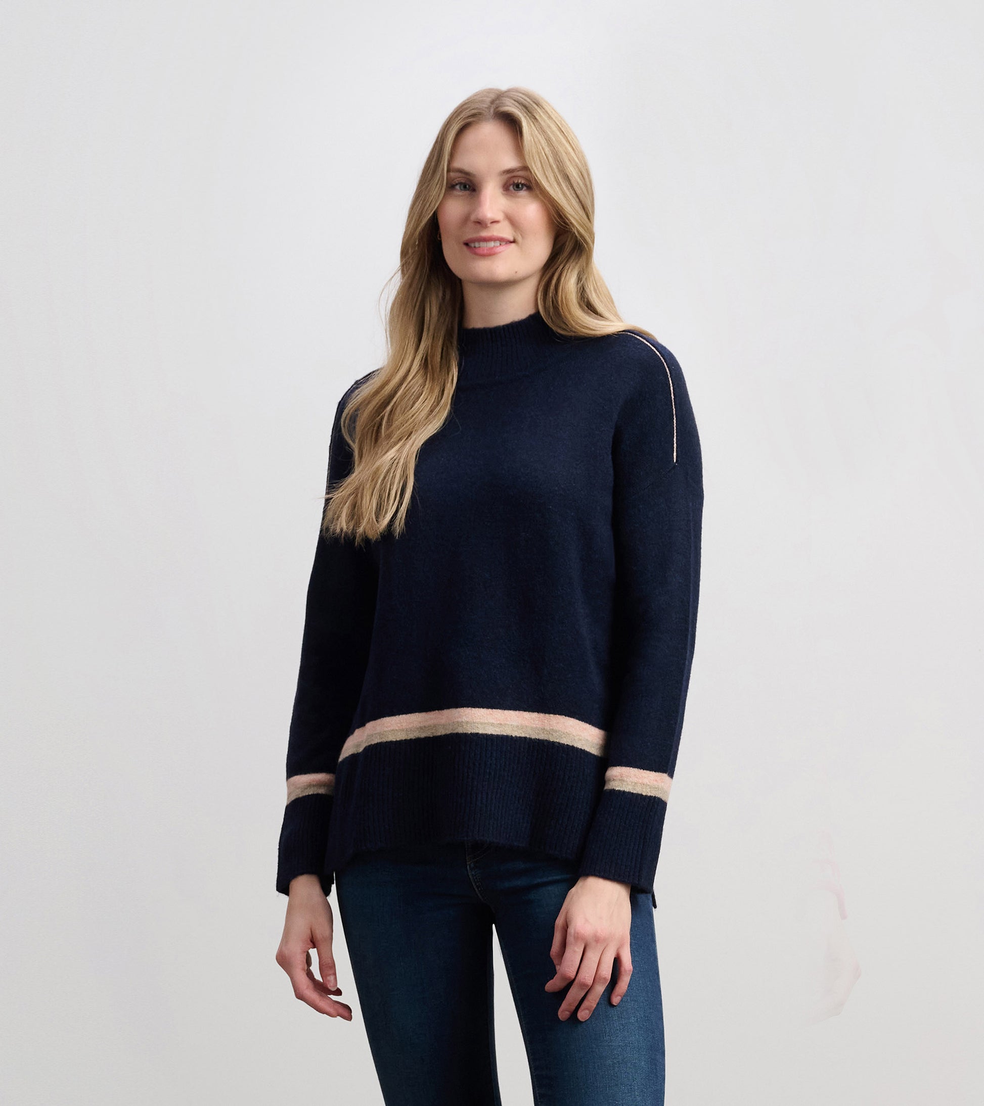 Navy mock neck sweater featuring a striped hem, long sleeves, and a relaxed fit, worn with blue jeans.