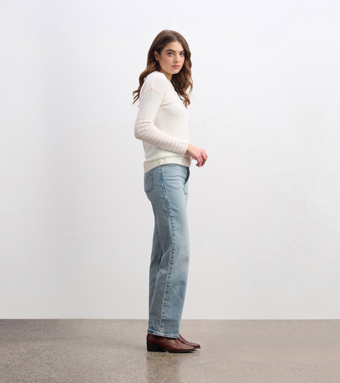 Cream sweater with long sleeves and striped detail, styled with light blue jeans and brown boots. Side view.