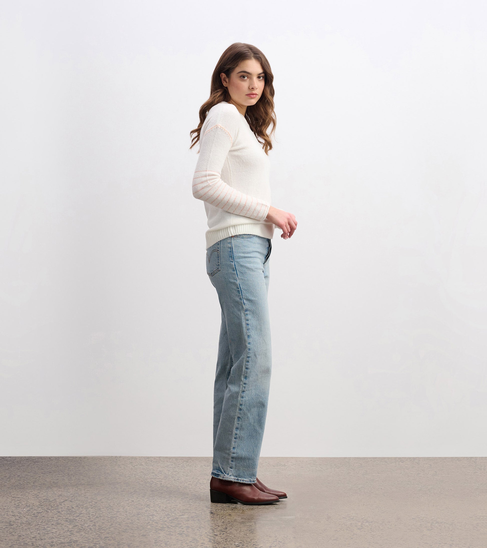 Cream sweater with long sleeves and striped detail, styled with light blue jeans and brown boots. Side view.