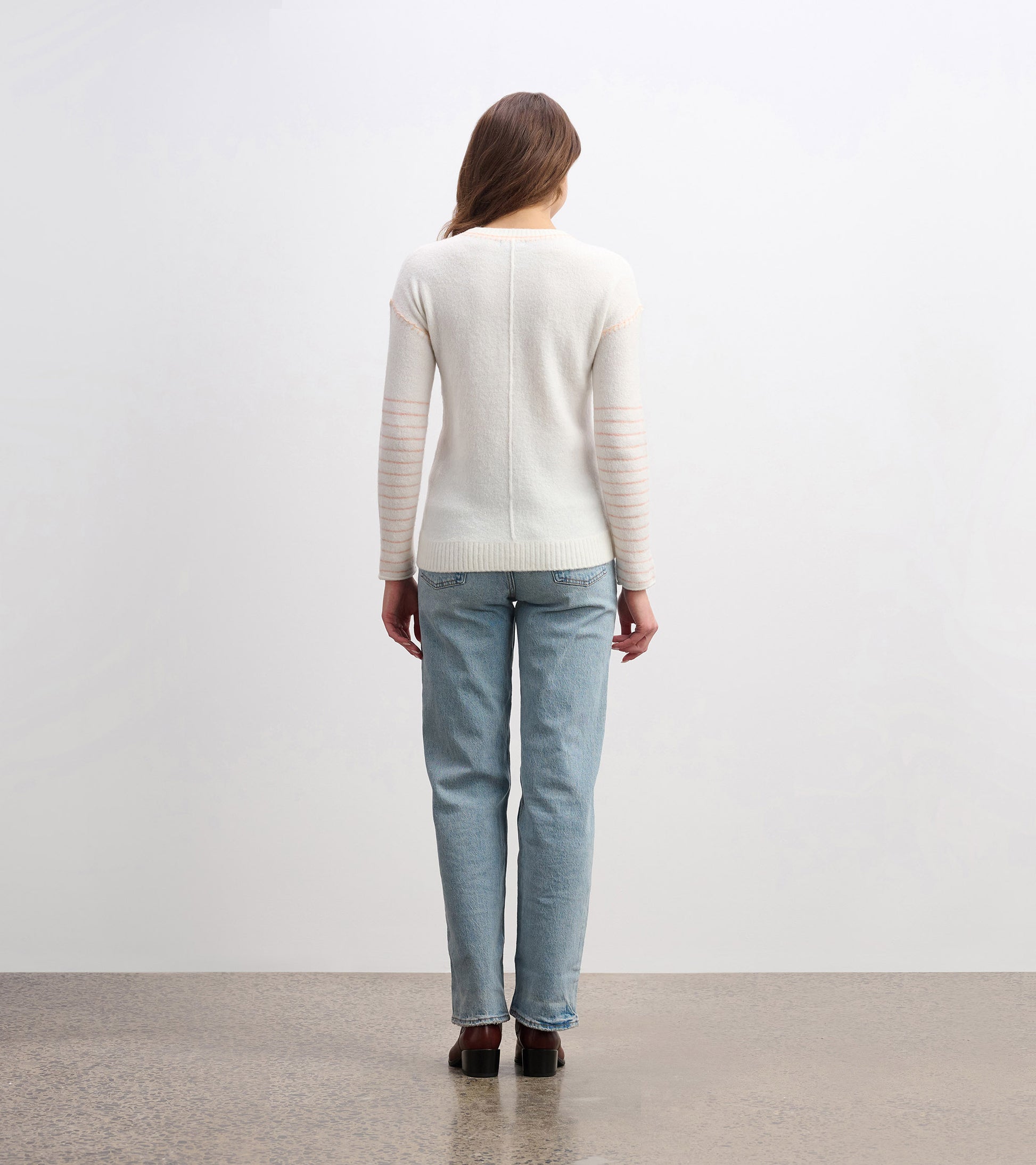Cream sweater with striped sleeves, fitted shape, and ribbed hem, shown from the back with light blue jeans.