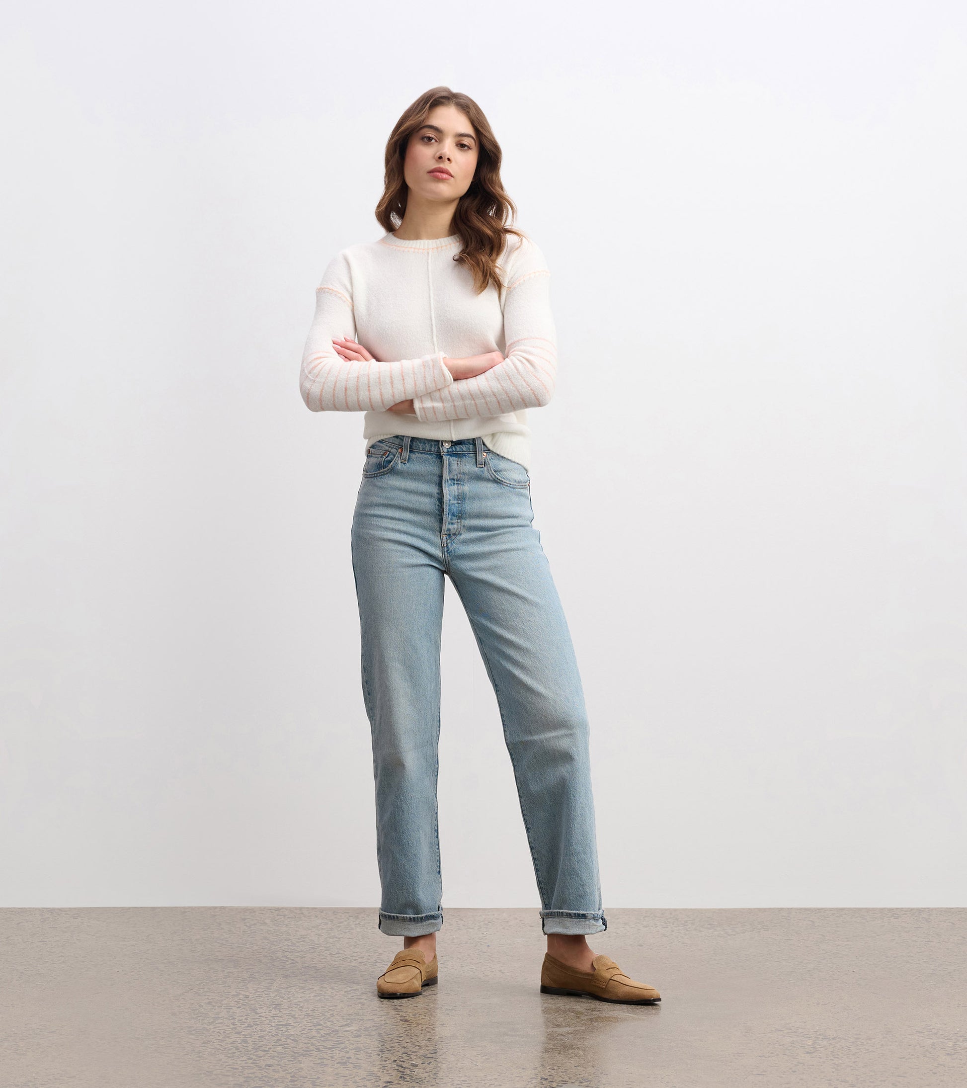 Cream sweater with subtle striped detailing, paired with light blue jeans, worn by a model standing confidently.