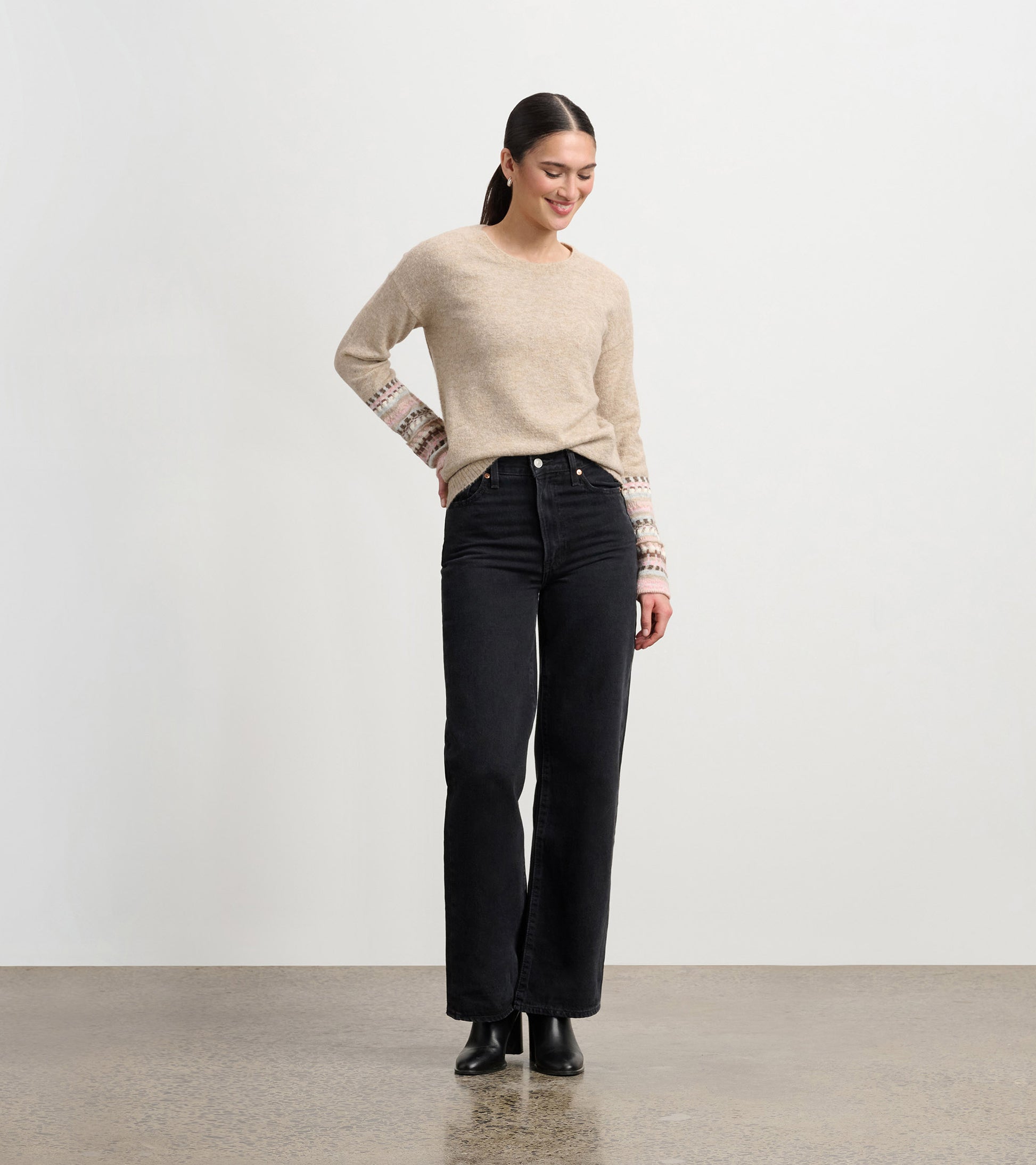Oatmeal melange sweater with patterned cuffs, paired with black high-waisted jeans, worn by a smiling model.