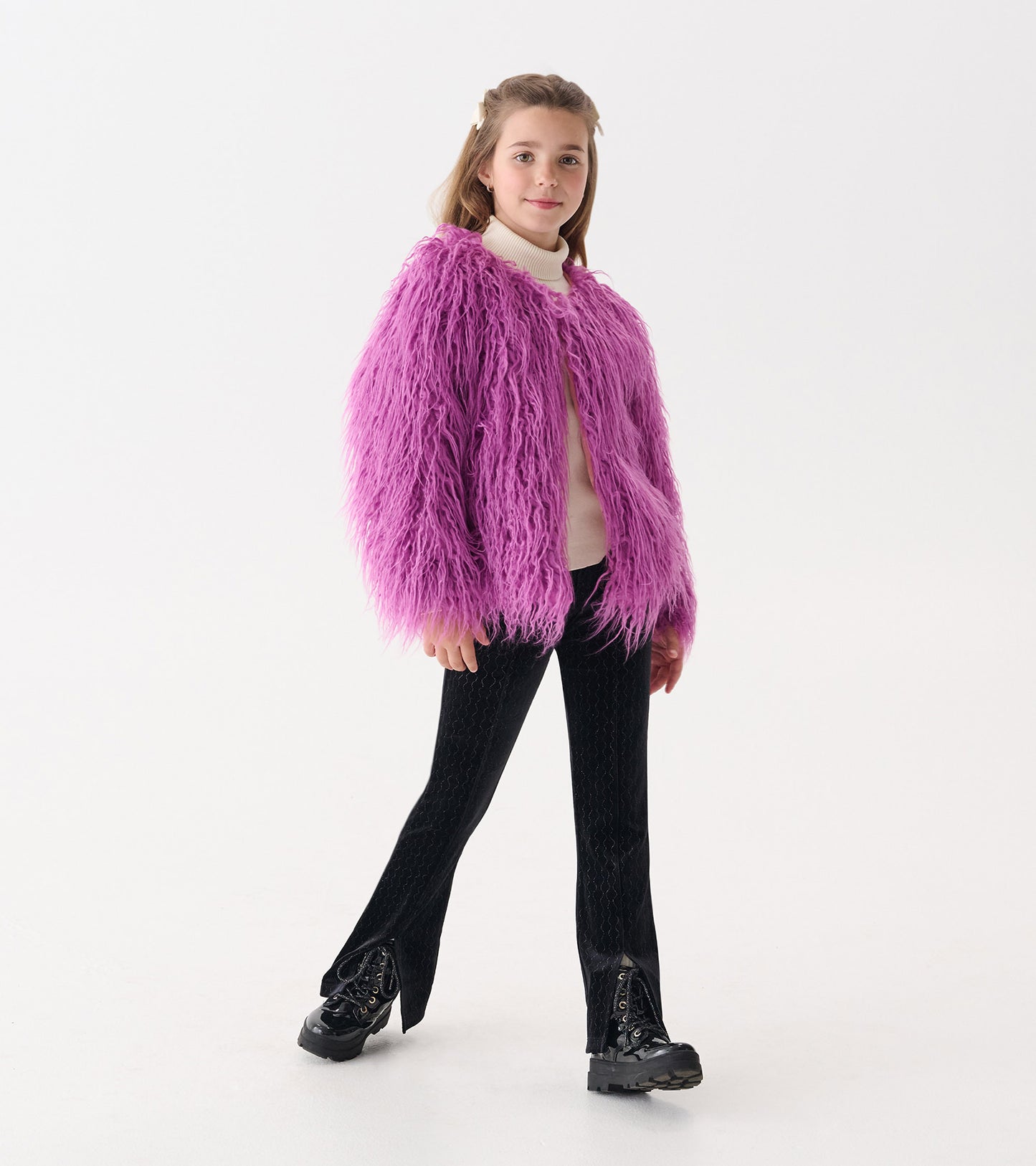 Purple Mongolian faux fur topper with long sleeves, worn over a light sweater and paired with black pants and boots.