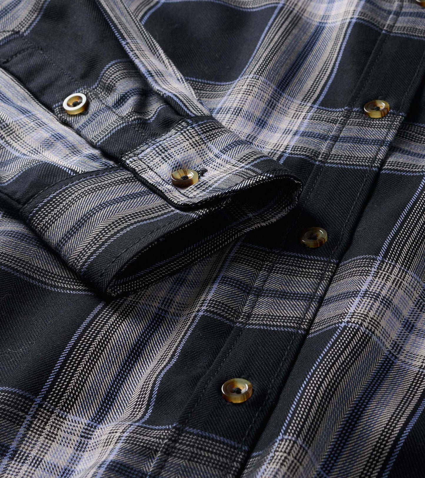 Close-up of black and tan plaid shirt dress showing button placket, collar, and rolled sleeve tab detail