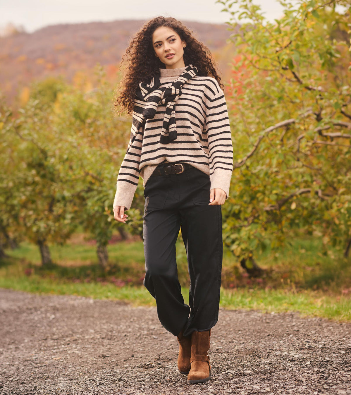 Women's black wide leg pants worn outdoors with a striped sweater, black belt, and brown ankle boots