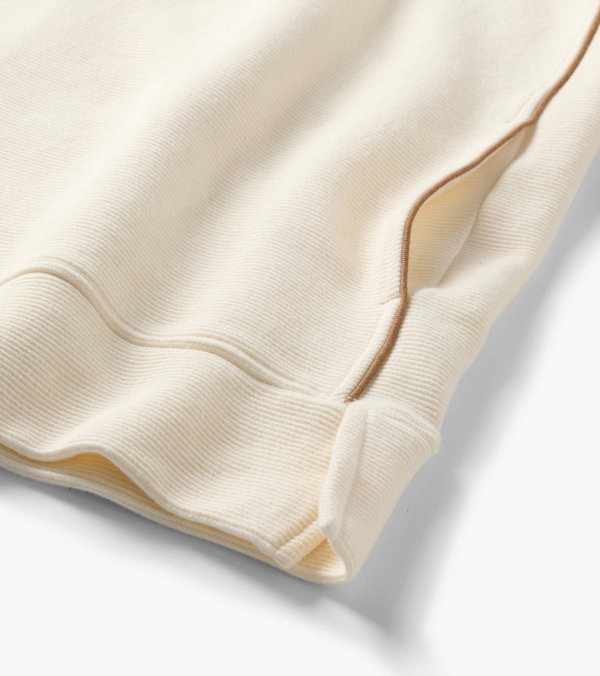 Close-up of the cream quarter-zip top showing fine ribbed texture and brown piping detail at the side seam