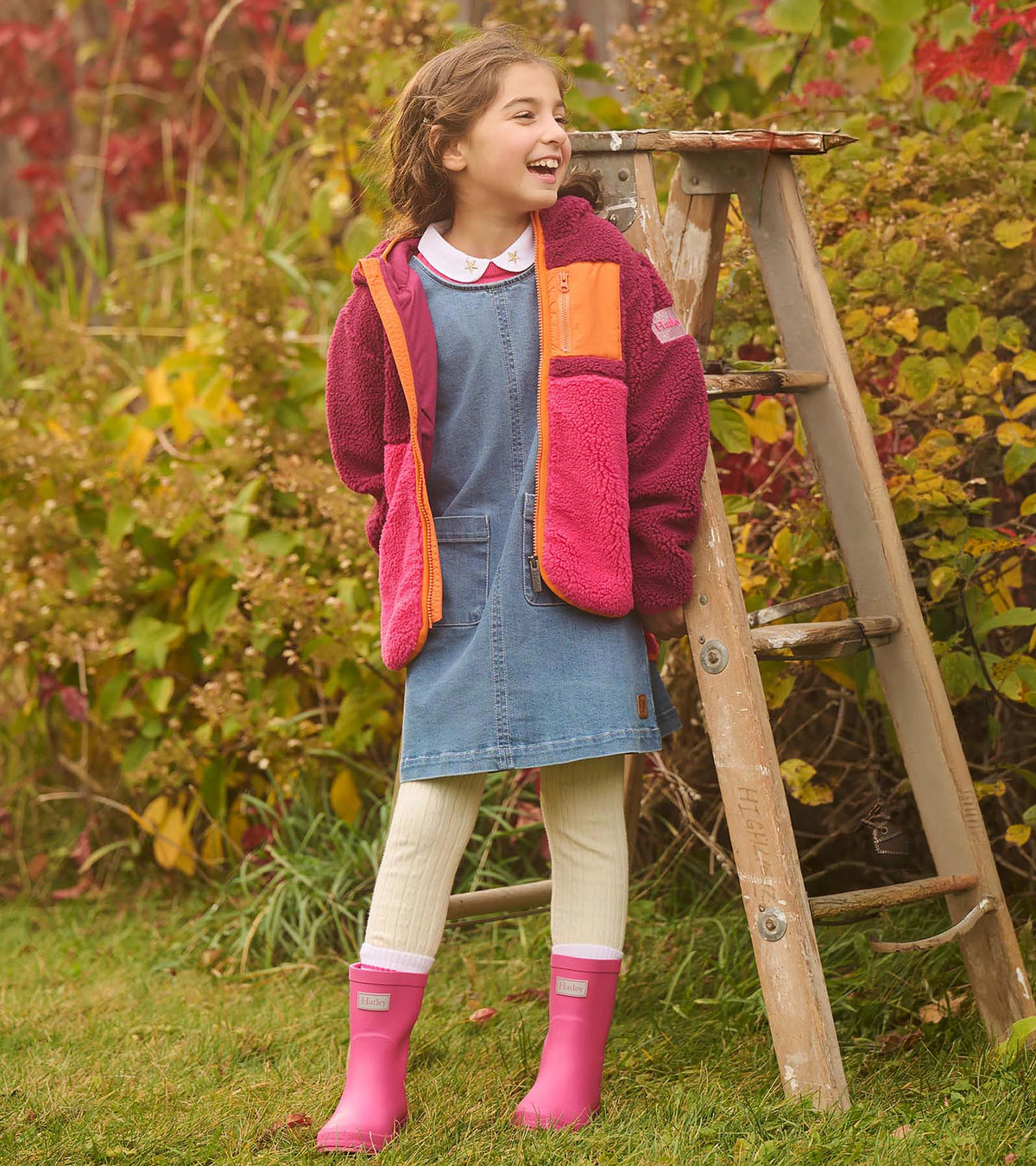 Girl wearing bright pink rain boots with a denim dress and color-block fleece jacket outdoors