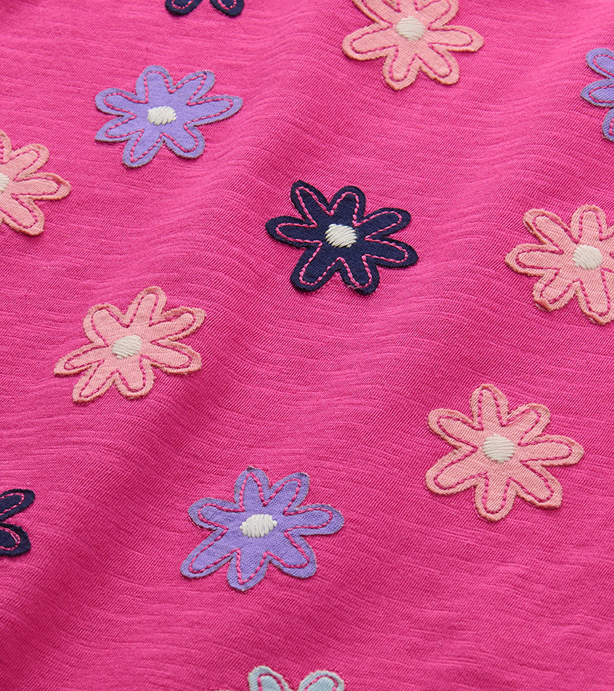 Close-up of pink T-shirt with embroidered flower graphics in pink, purple, light blue, and navy