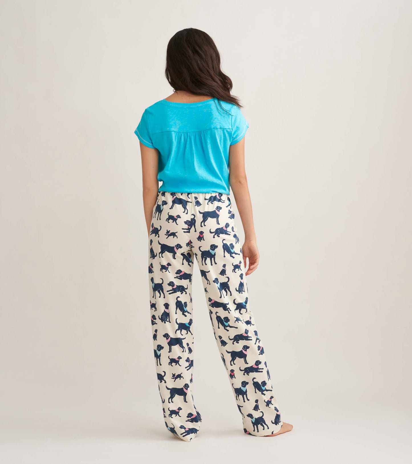 Women's cotton pajama pants featuring a playful dog print on a cream background, shown from the back.