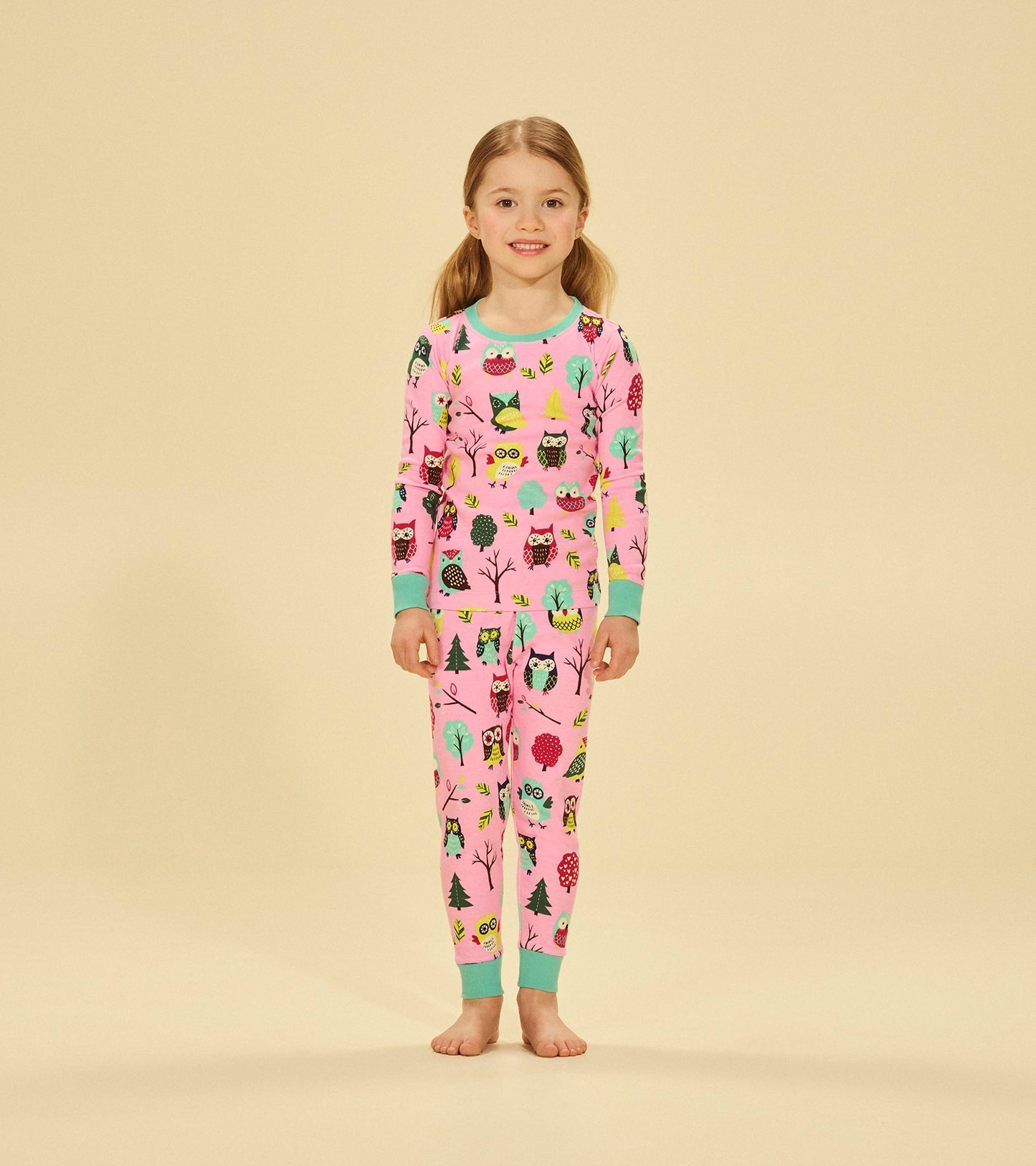 Pink pajama set featuring colorful owl and tree patterns, with long sleeves and matching pants, suitable for kids.
